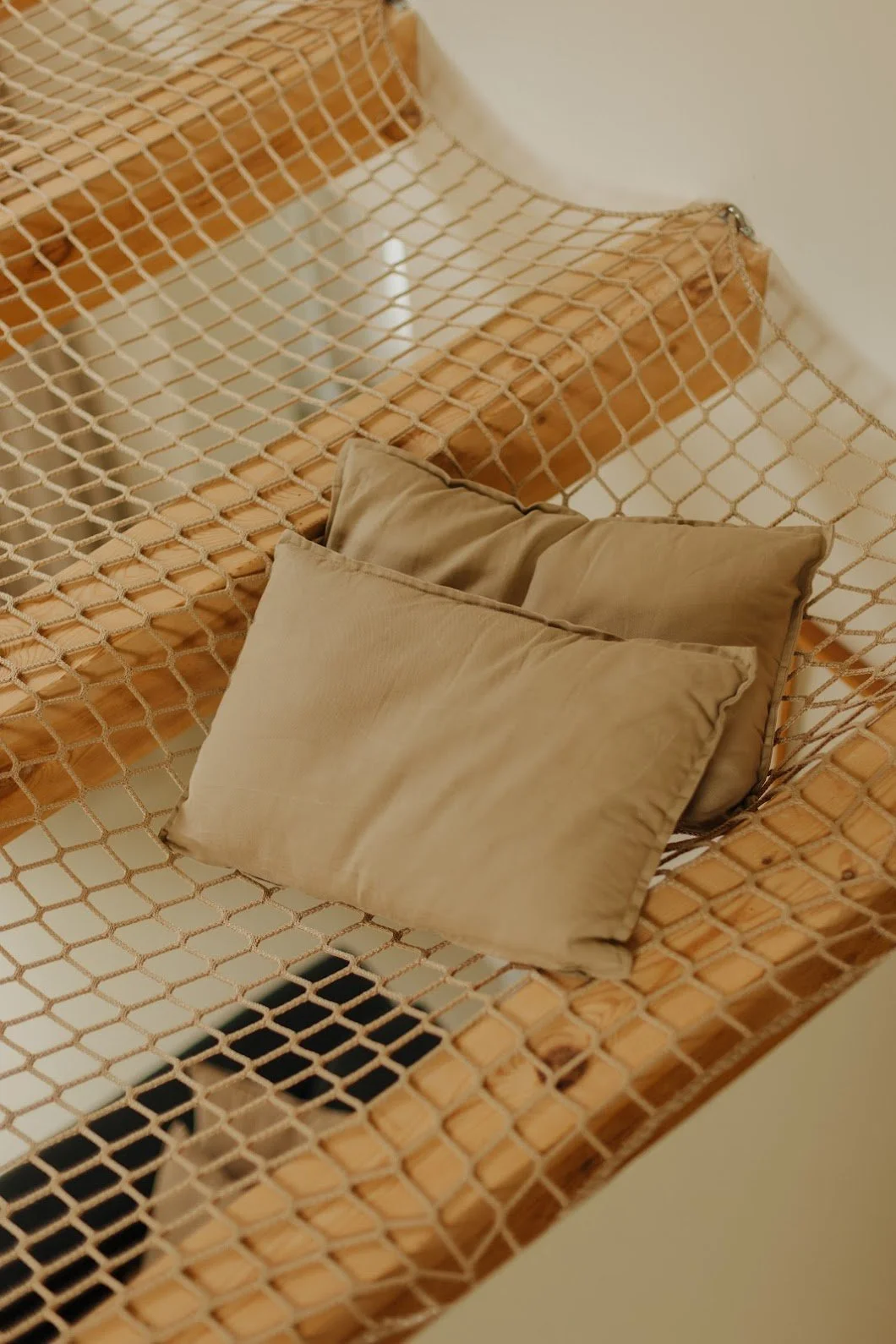 A modern wooden sofa with a mesh backrest and seat, adorned with three beige cushions.