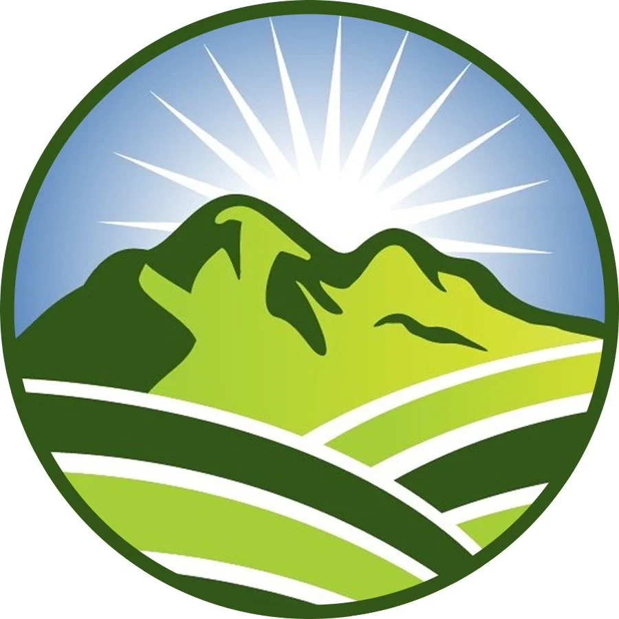 An illustrated logo with green mountains, sun rays behind the mountains, and rolling fields in the foreground, enclosed in a circular green border.