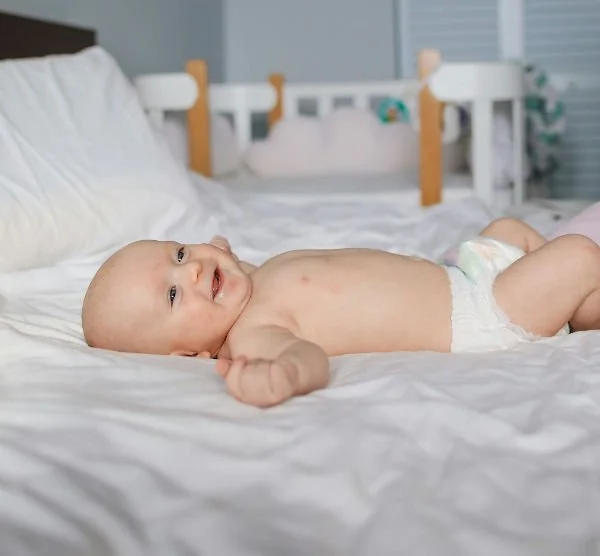 smiling-baby-laying-on-bed-wearing-nappy-small.jpg