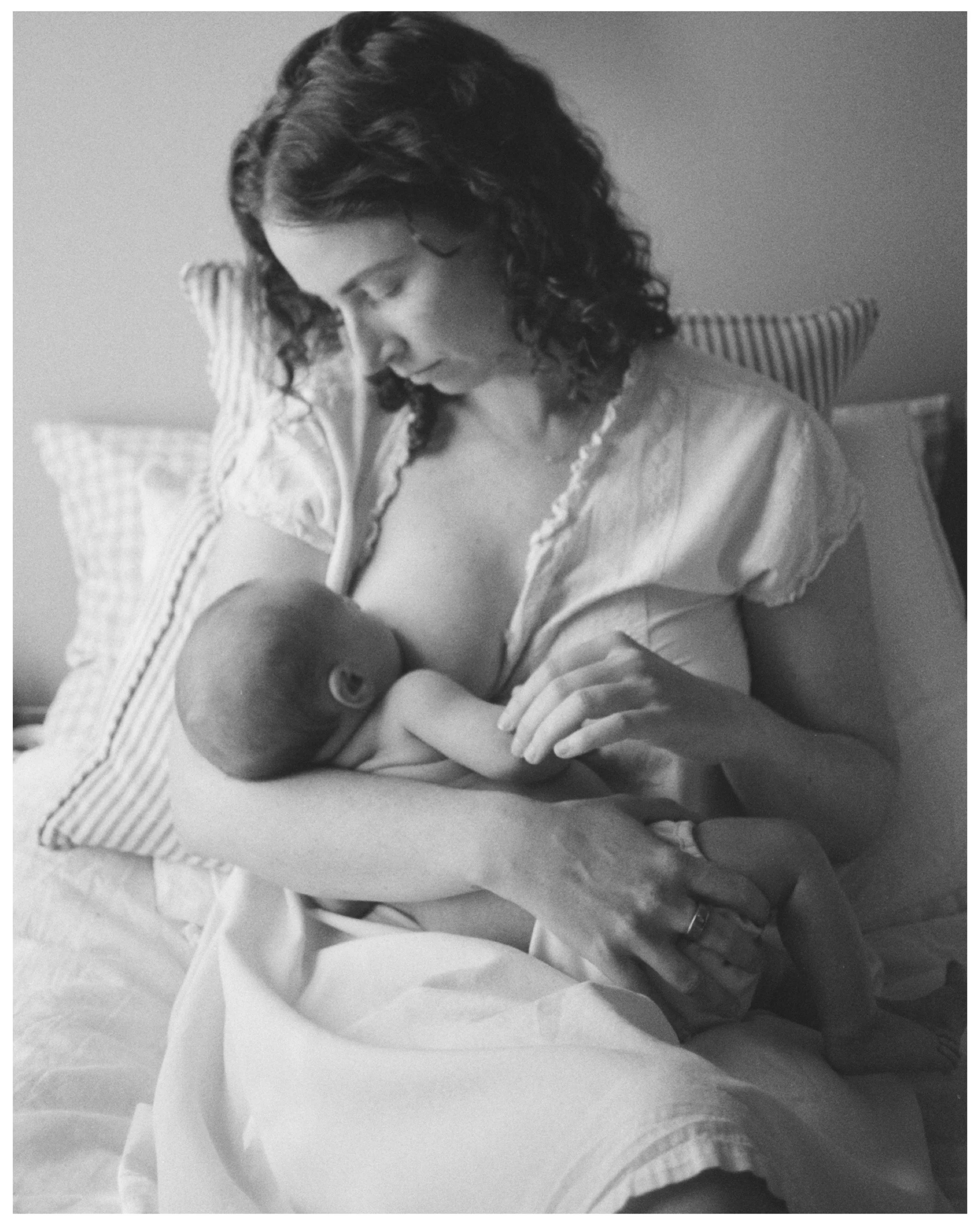 A woman breastfeeding a baby with a striped pillow behind her head.