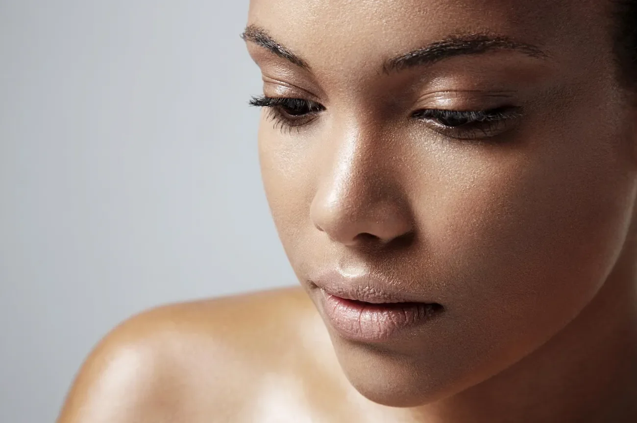 Close-up of a woman with smooth, glowing skin, looking downward.