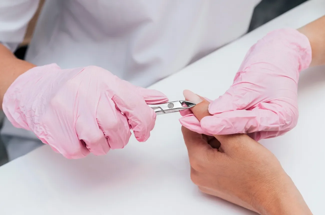 A person with pink gloves is trimming a person's fingernail with manicure scissors.