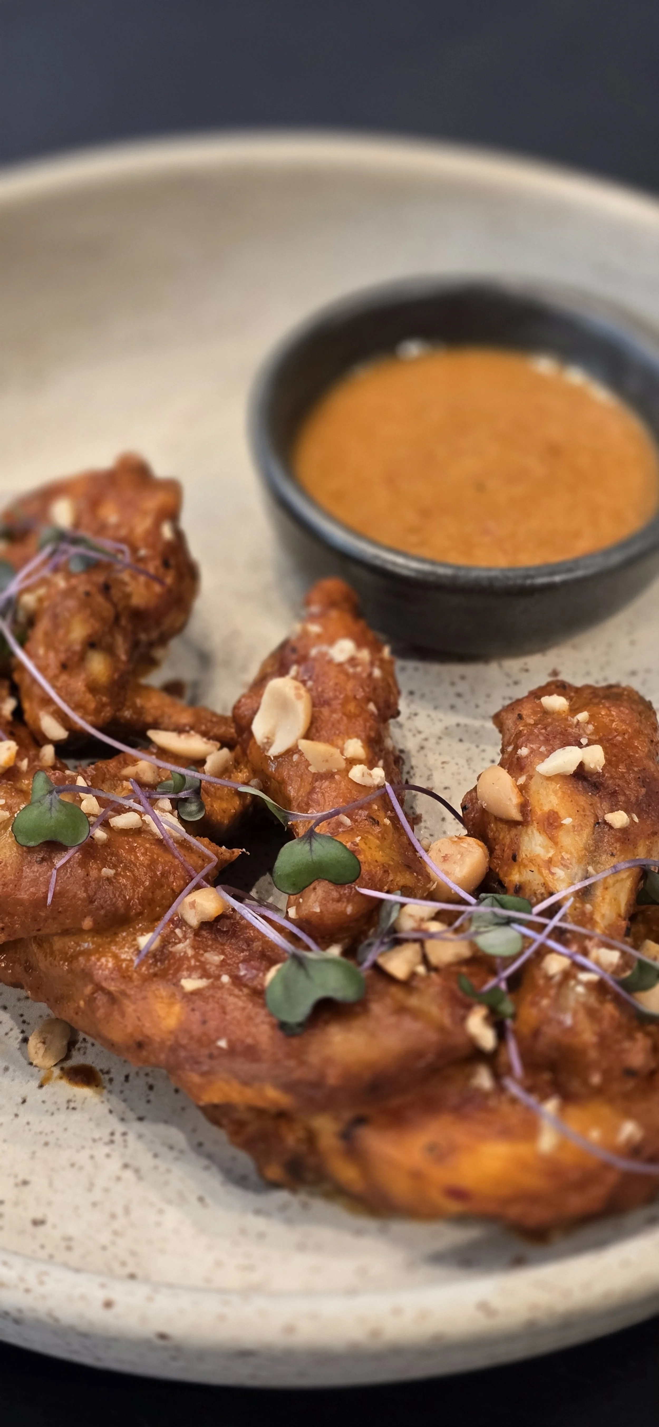 Crispy suya chicken wings with roasted peanut garnish and dipping sauce at WeRise Wine Bar.