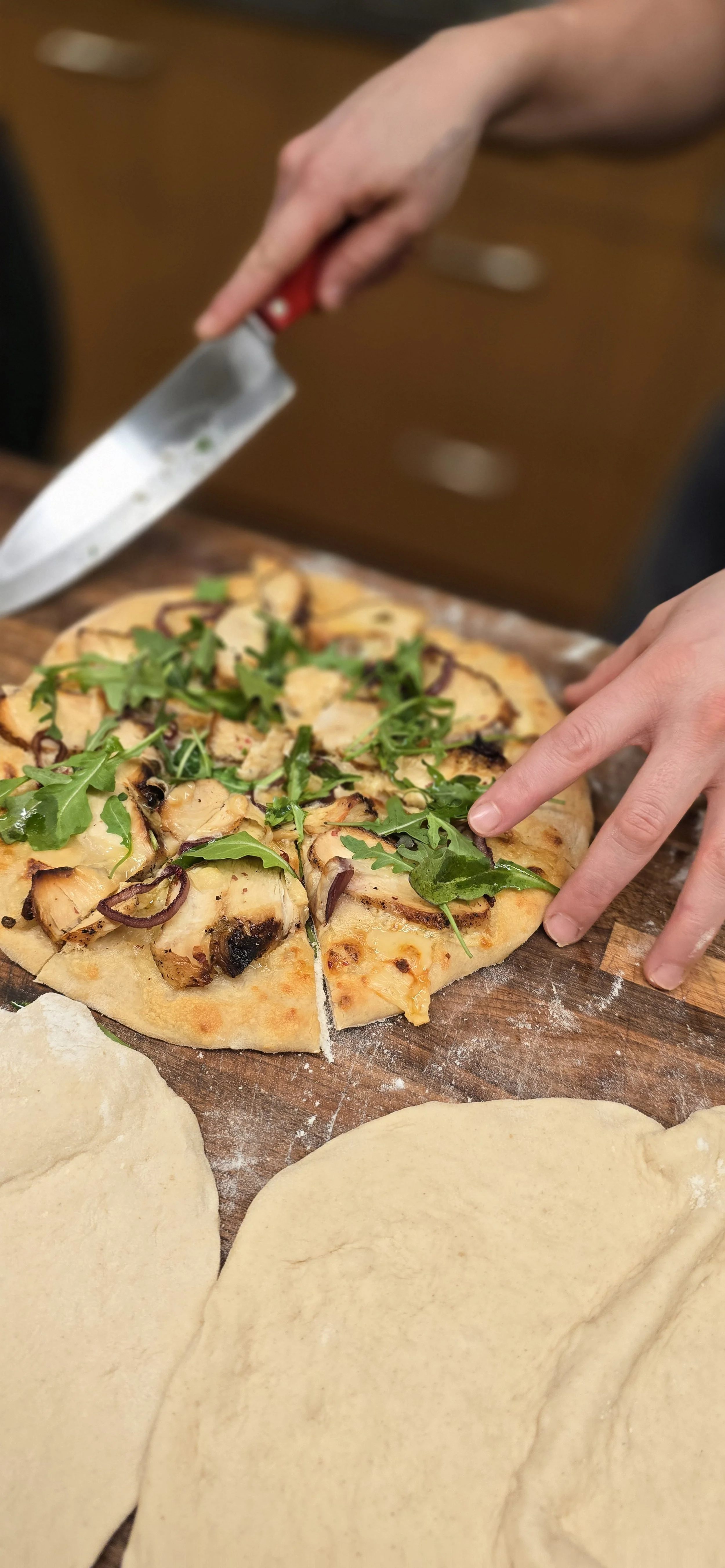 Freshly baked flatbread pizza with arugula, onions, and grilled chicken being sliced at WeRise Wine Bar.