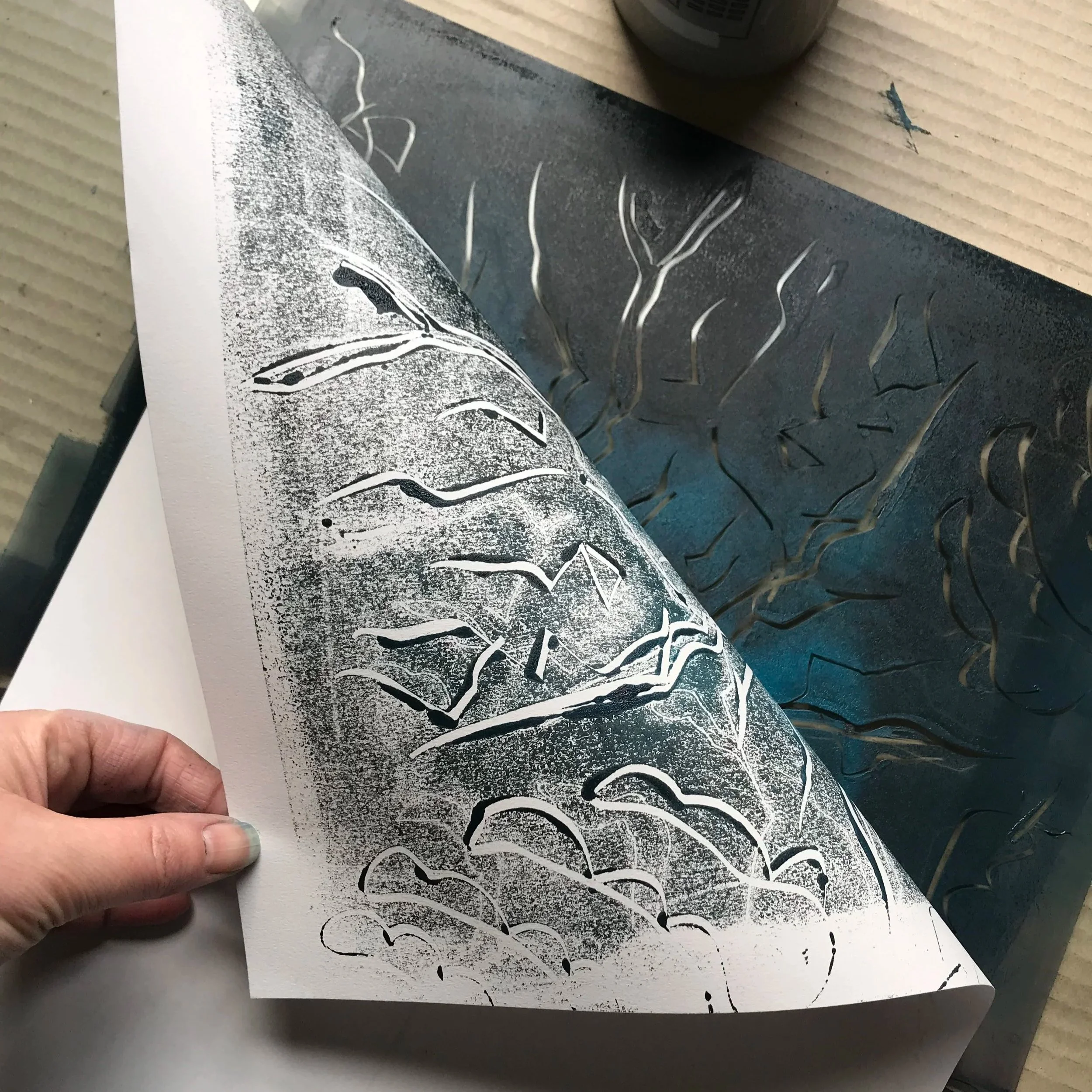 the artists hand peeling back a piece of paper from the printmaking plate