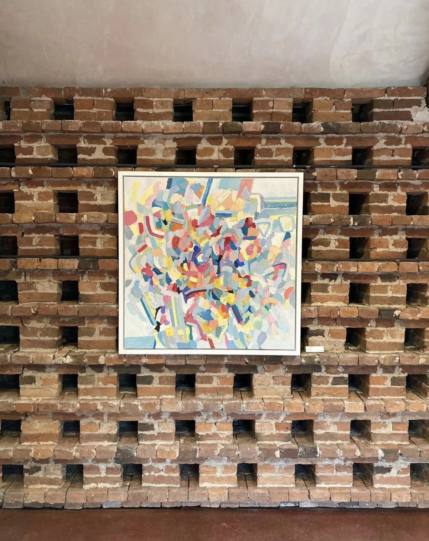 Abstract oil painting by Liz Foster hanging against a rustic brick wall 