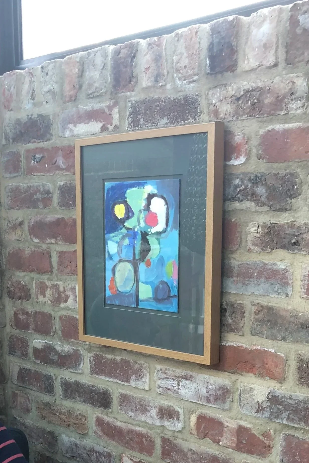 small abstract oil painting hanging on an exposed brick wall in a modern kitchen 