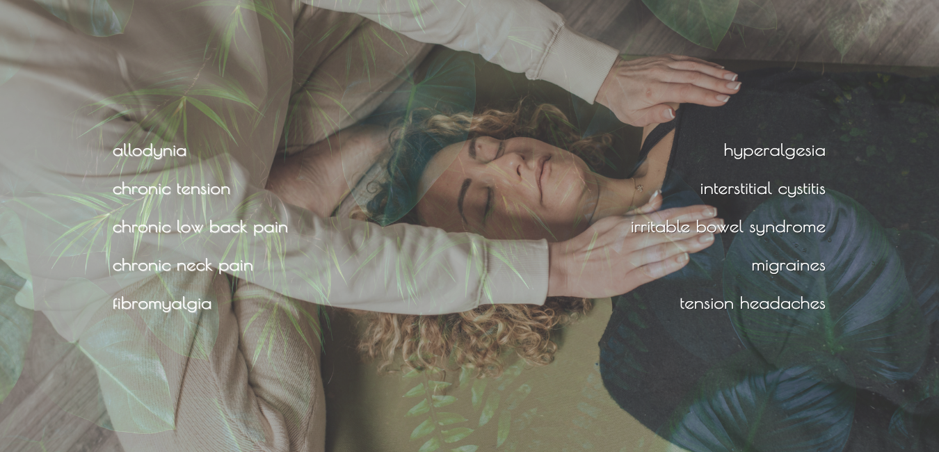 Woman lying on back receiving a clothed somatic healing and trauma-informed massage while another woman gently places her hands on her shoulders