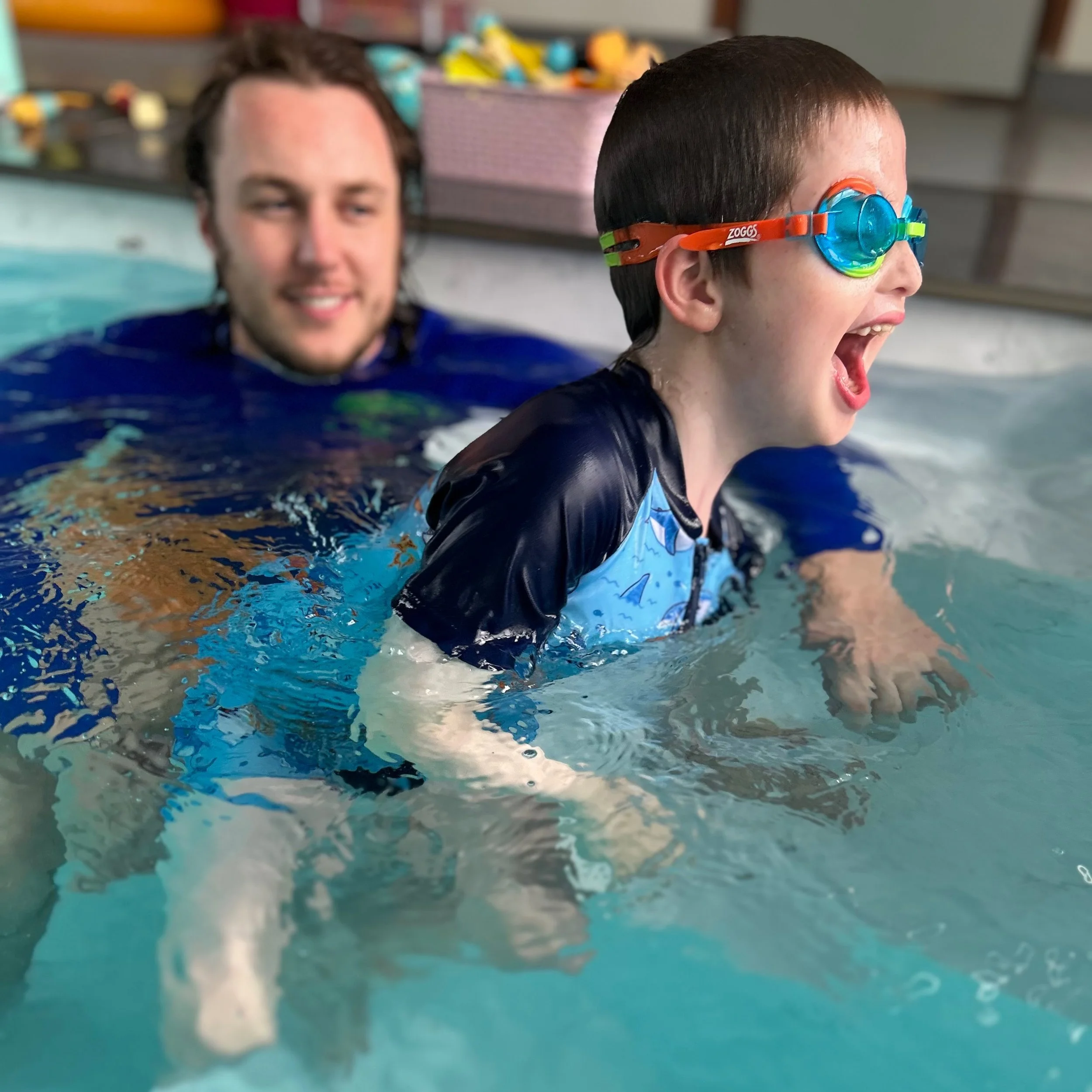 SEND swimming lessons: a Happy Fins teacher laughing with a young swimmer in goggles