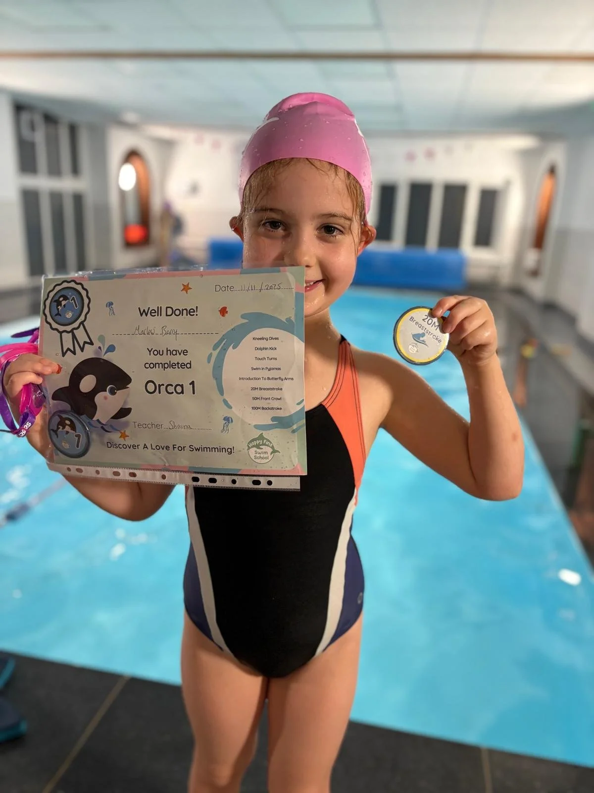 A proud young swimmer holds up her award scheme certificate and badge by the pool