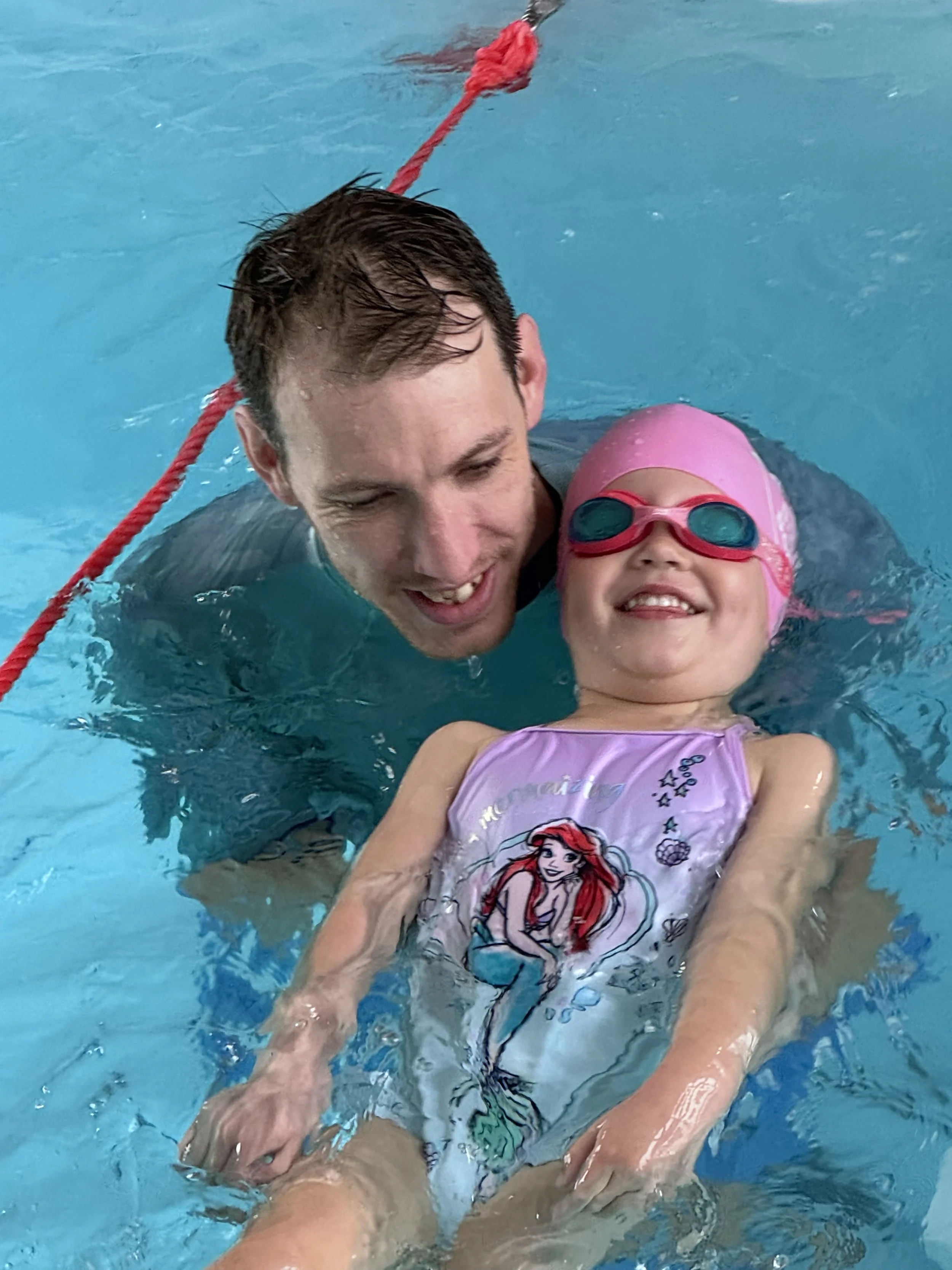 A Happy Fins teacher supports a young swimmer as they float on their back