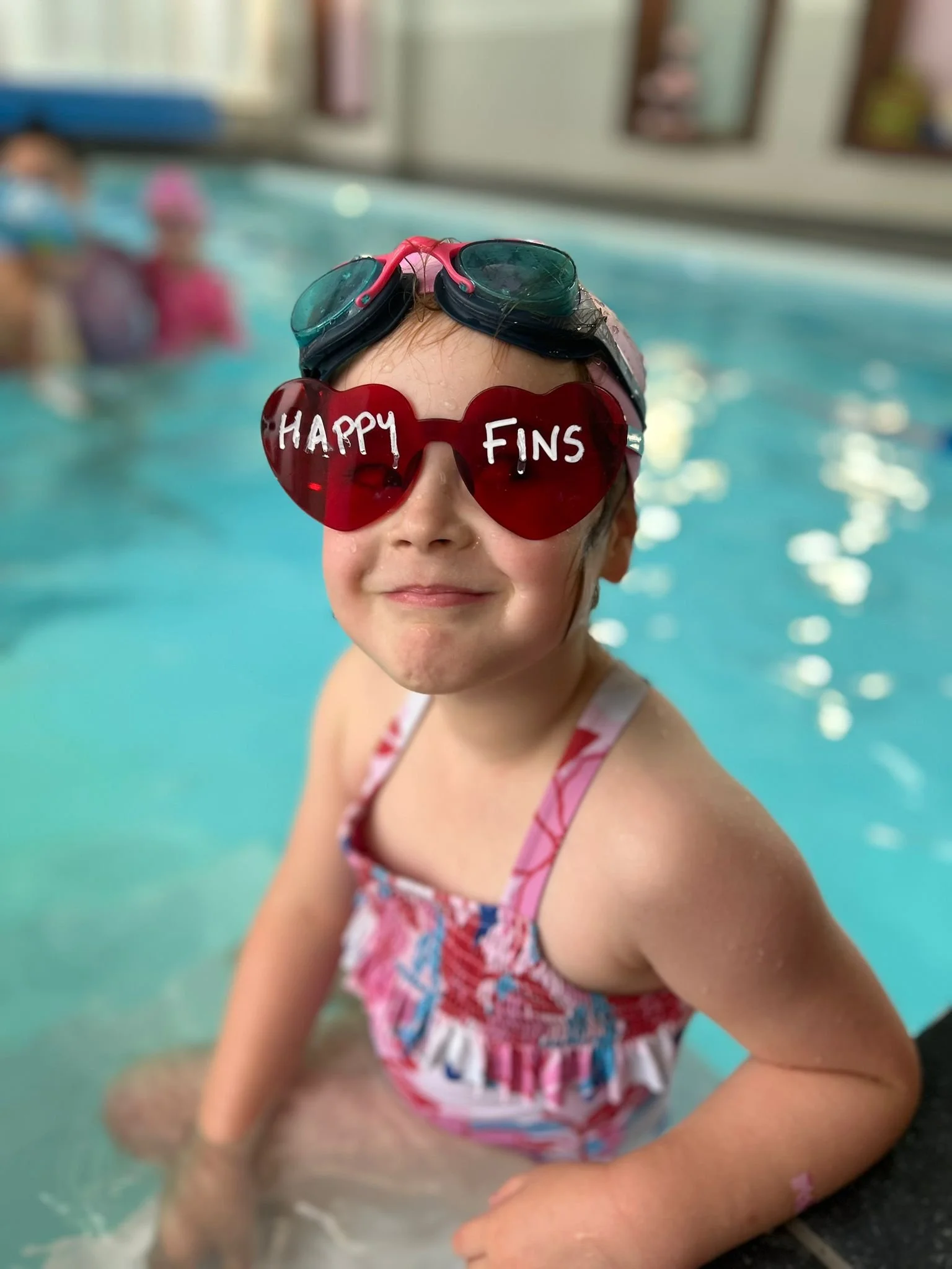 1-to-1 and 2-to-1 swimming lessons: a smiling young swimmer in heart-shaped Happy Fins glasses in the pool