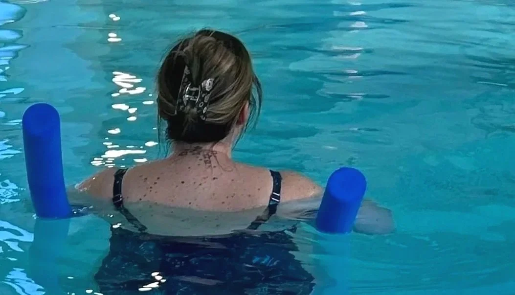 Aquanatal classes: a woman exercises with foam noodles in an aquanatal class