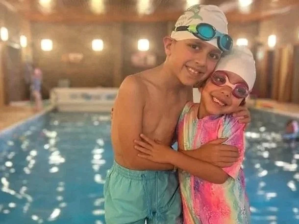 Two young swimmers share a hug by the pool