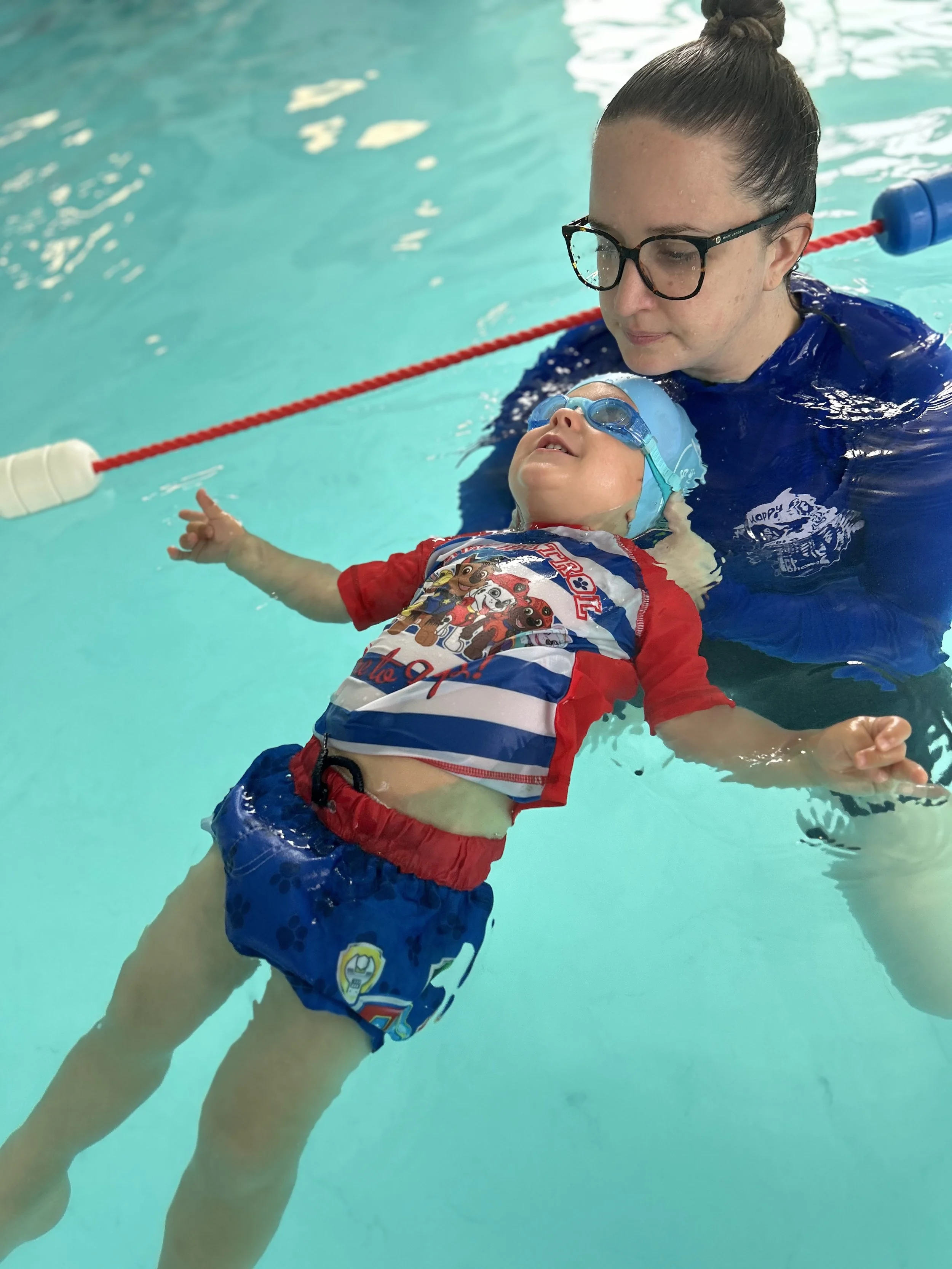 A Happy Fins teacher supports a toddler floating on their back