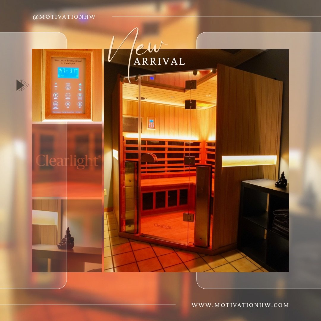 A wooden infrared sauna with glass door and seating inside, located in a room with tiled floor, next to black shelving unit with towels, illuminated by warm lighting.