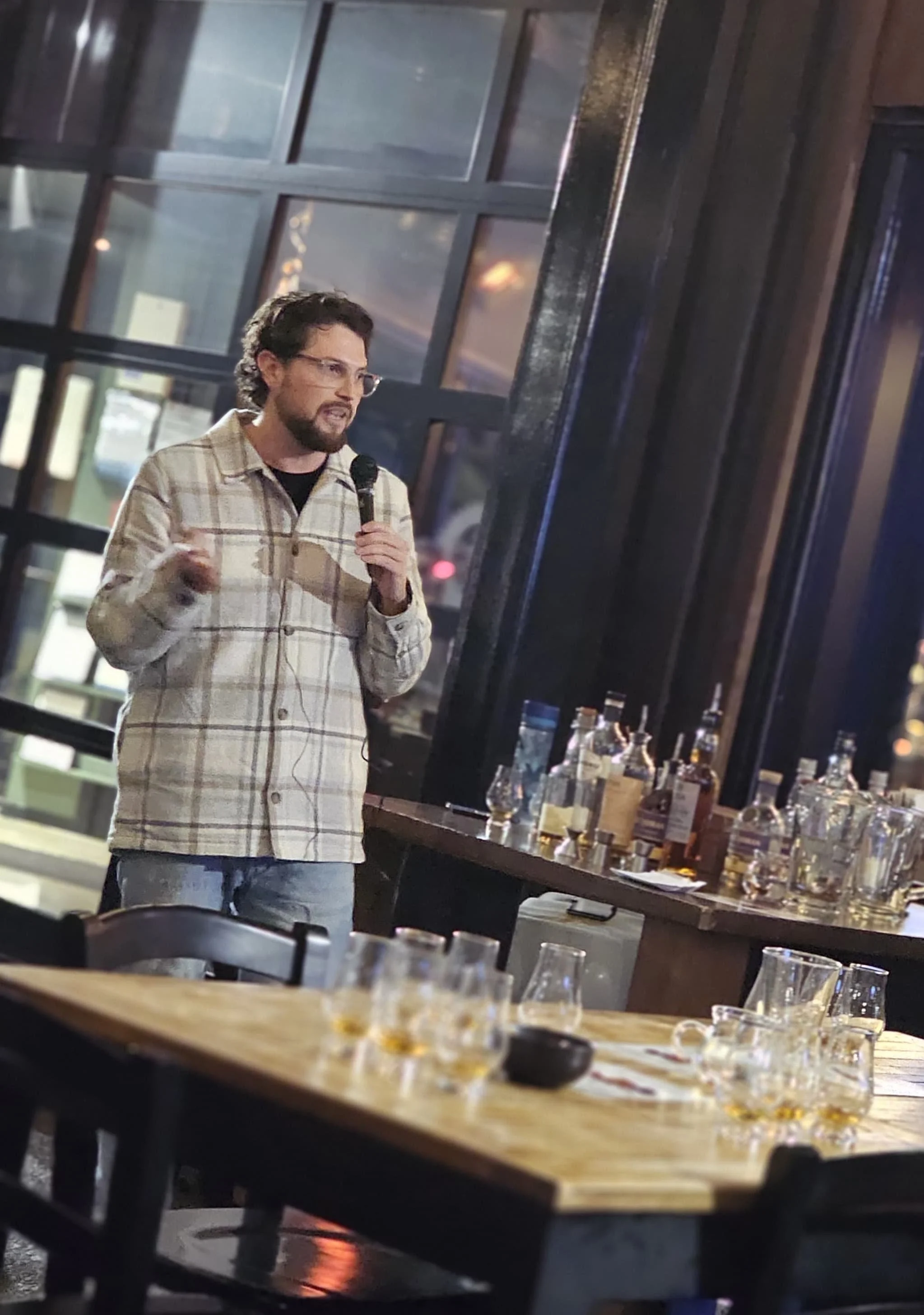 Person with microphone in bar setting, bottles on table