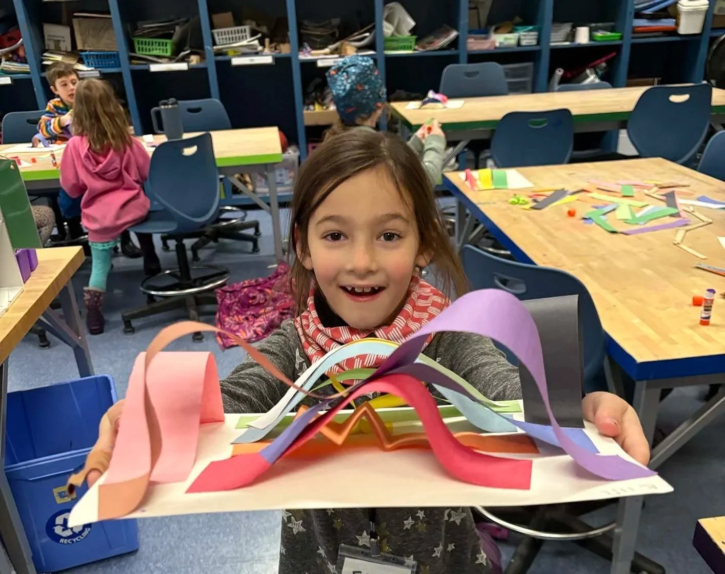 A young child holding up a 3D art project, constructed from craft paper.