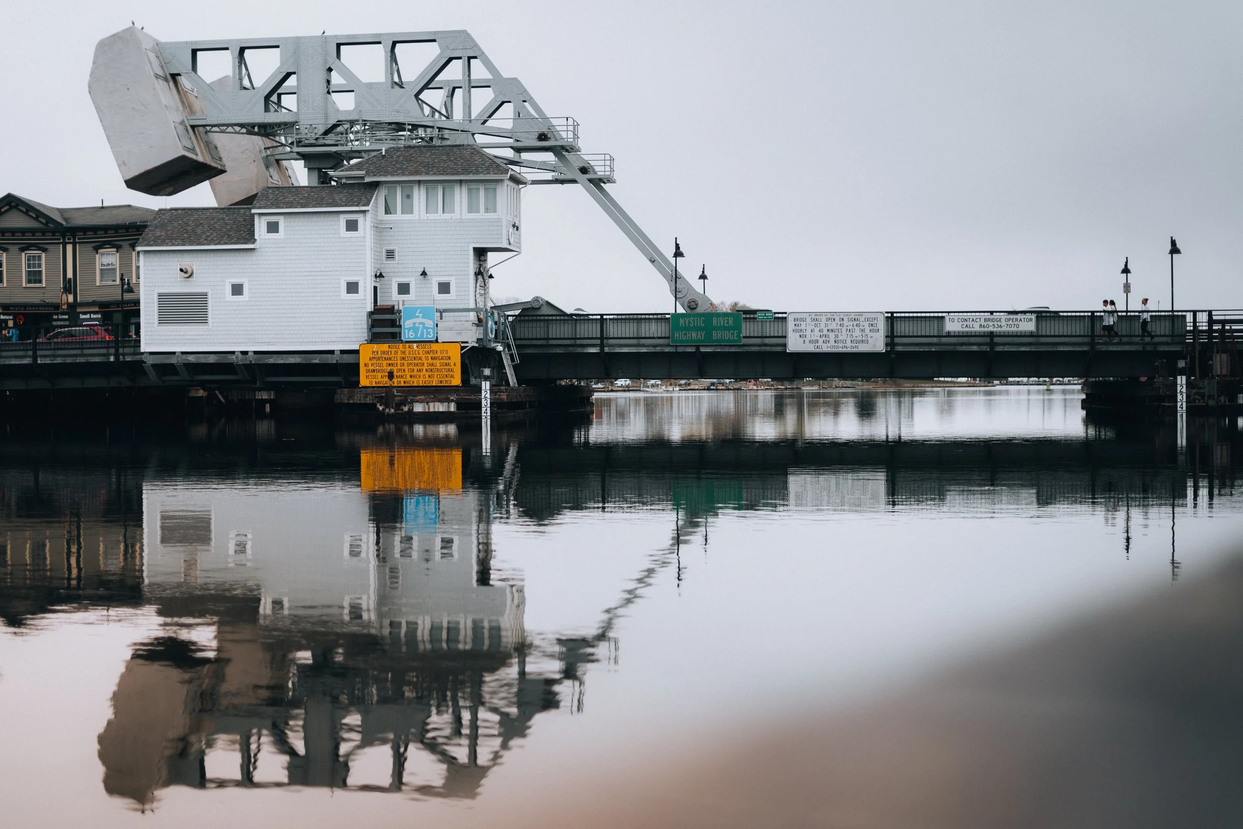 A bridge over a body of water with a large mechanical lift system, white building structure on the bridge, and reflections in the water.