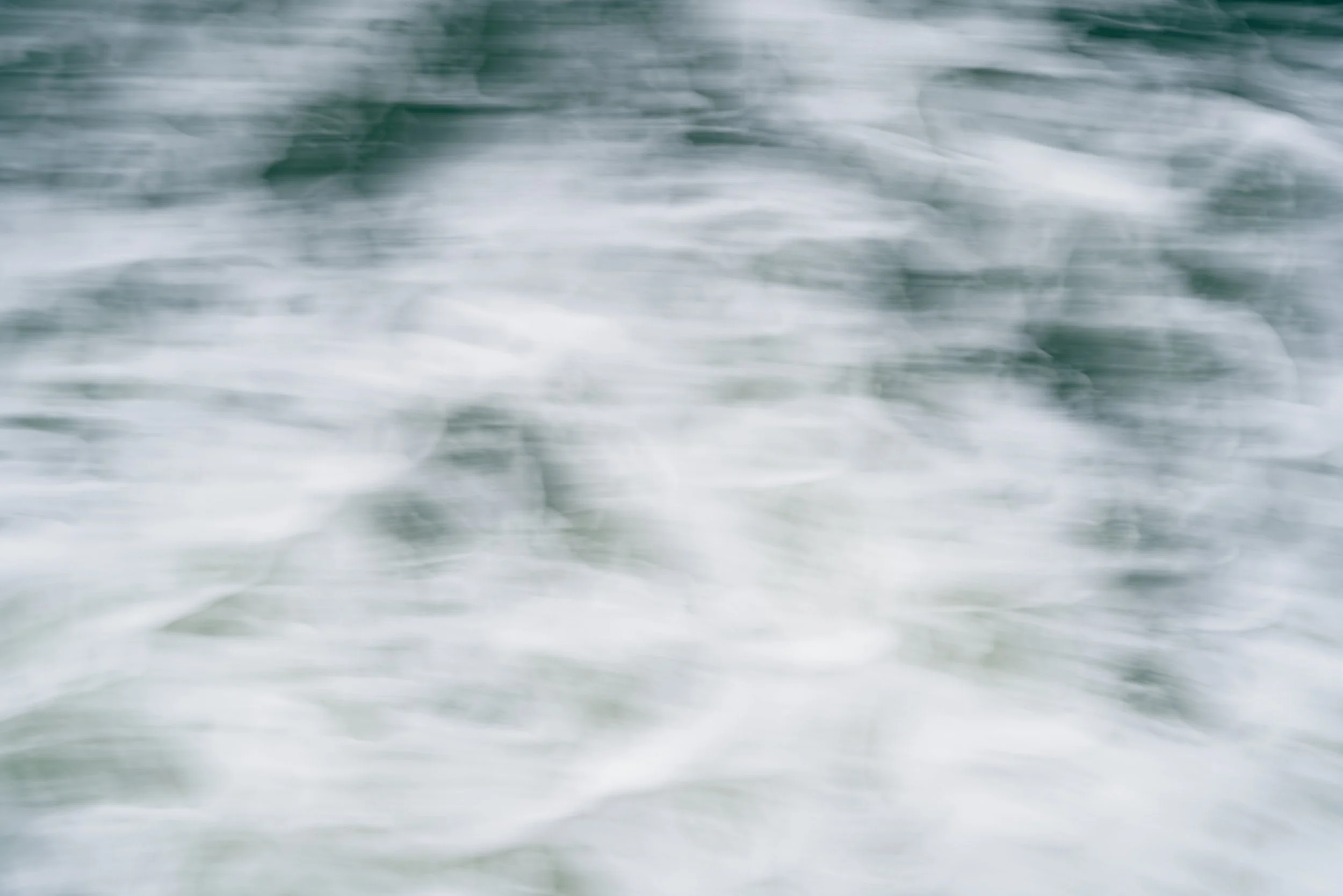 Blurred image of ocean waves with white foam and greenish-blue water.