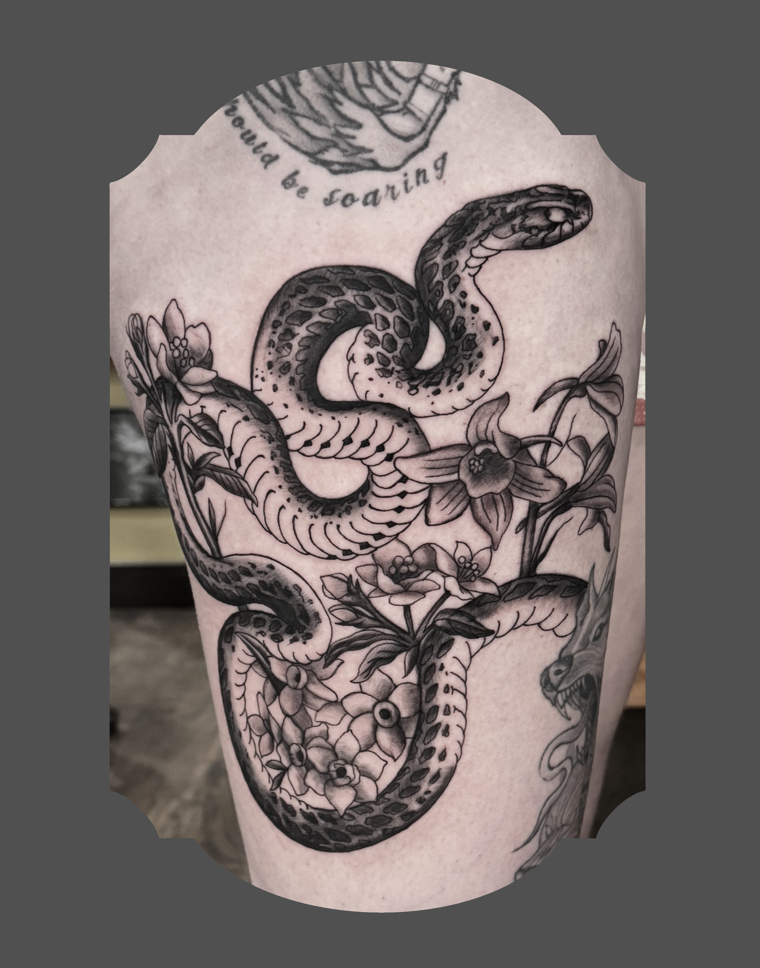 Black and grey tattoo of a coiled snake surrounded by flowers on a person's skin.