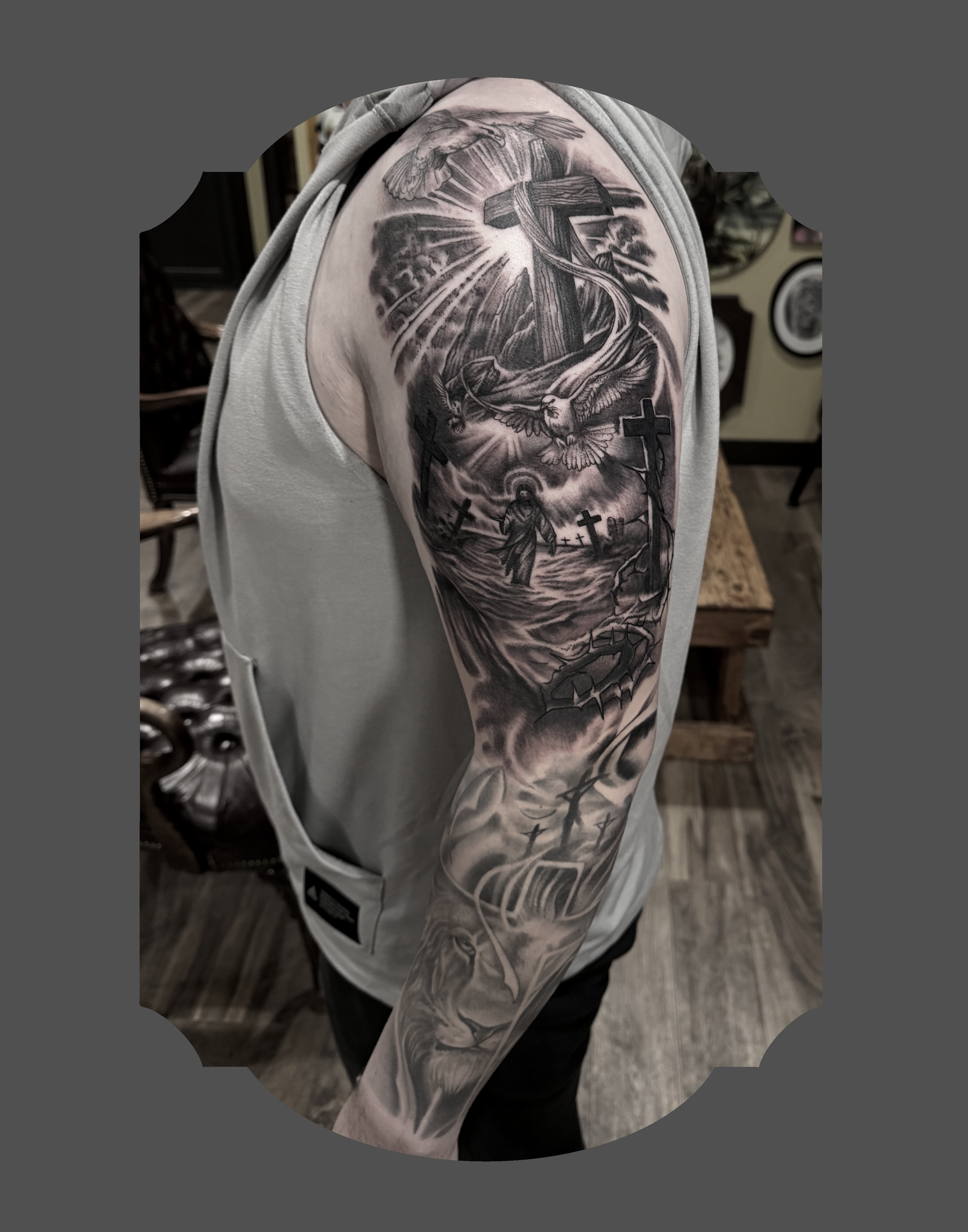 Black and grey tattoo sleeve depicting a cross, a person at the foot of the cross, a dove, and rays of light, with a church or religious buildings in the background.