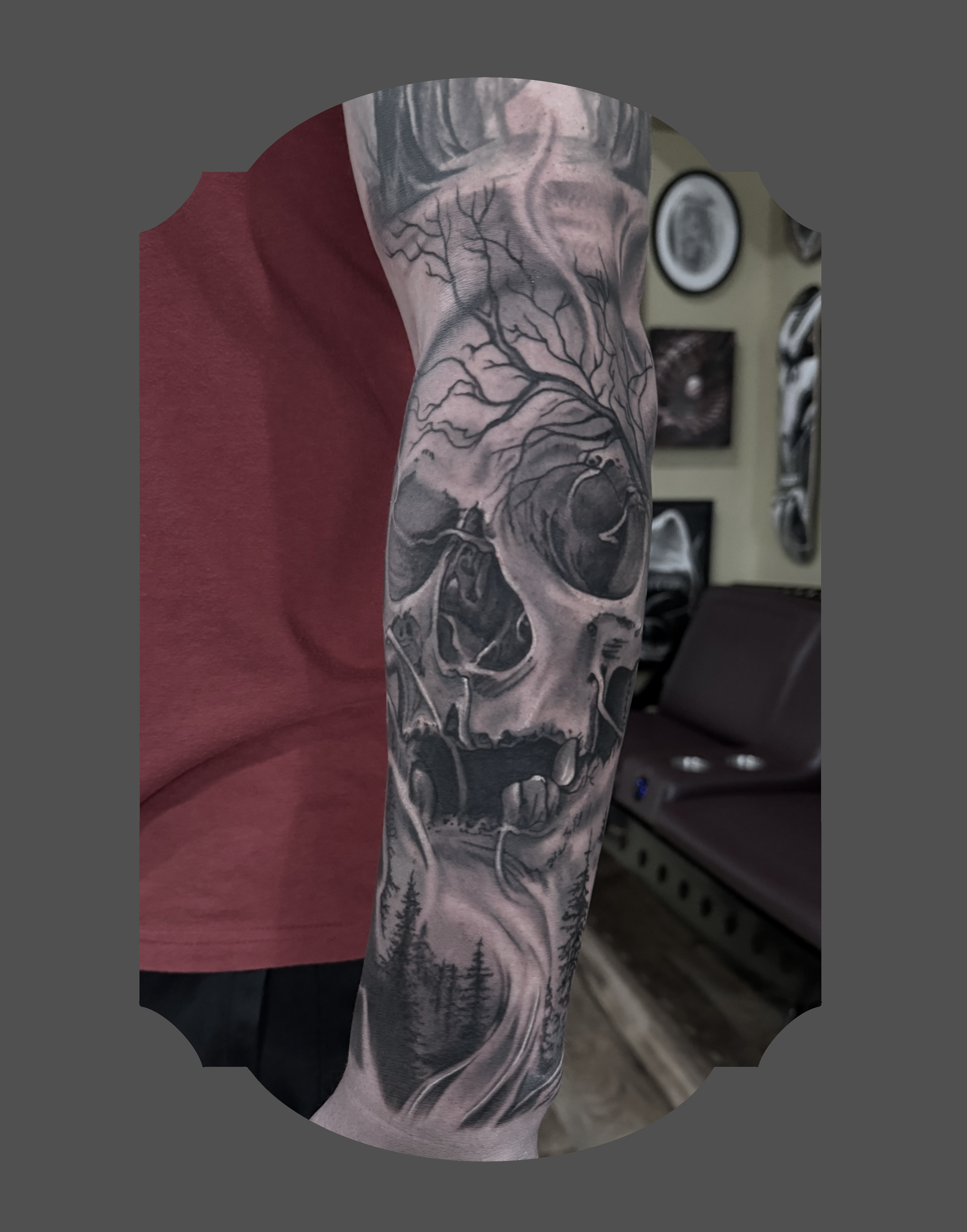 Tattoo sleeve featuring trees, skulls, and a wolf on a person's arm, with a background of trees and mountains.