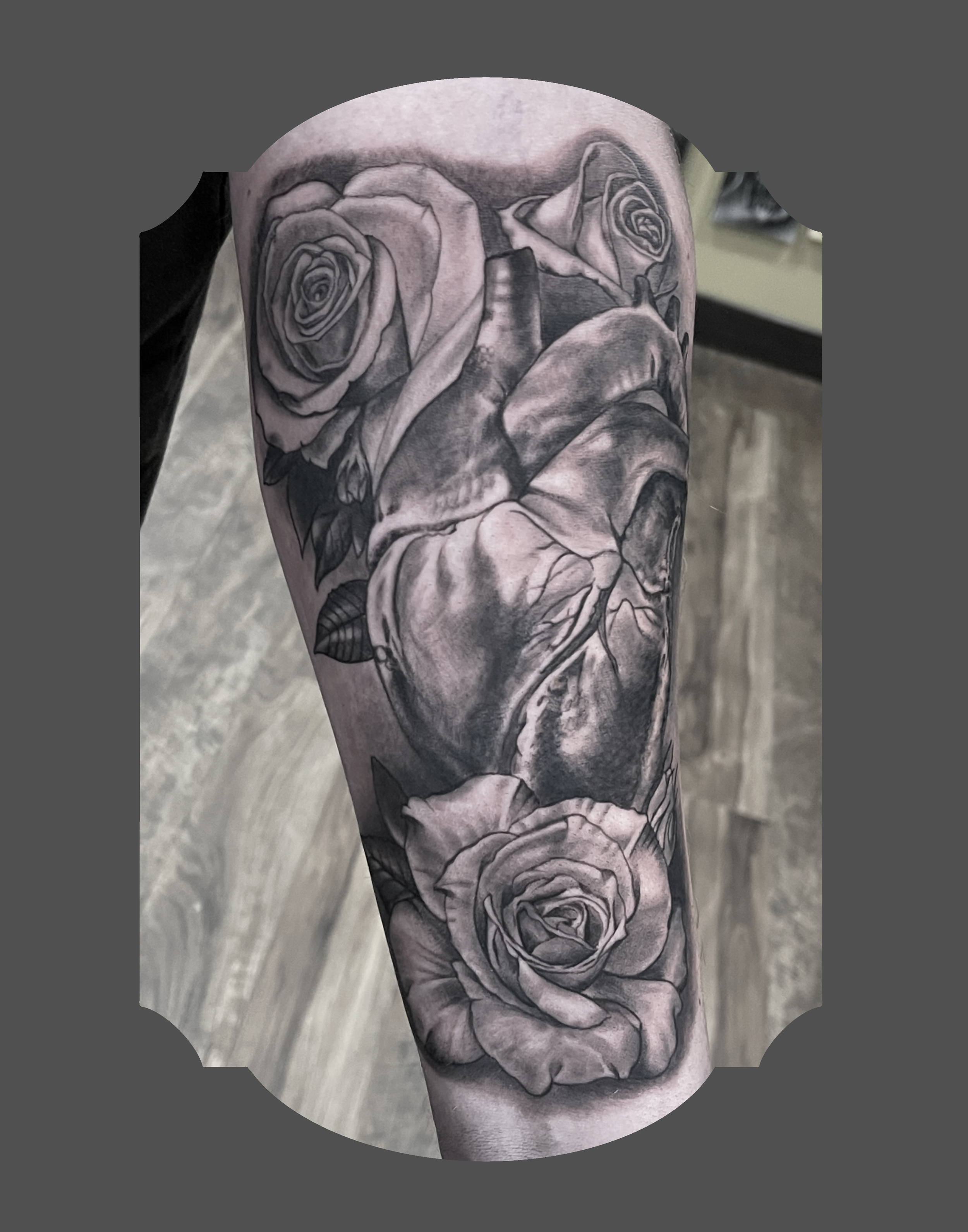 Black and gray tattoo of roses and a realistic heart on a person's arm.