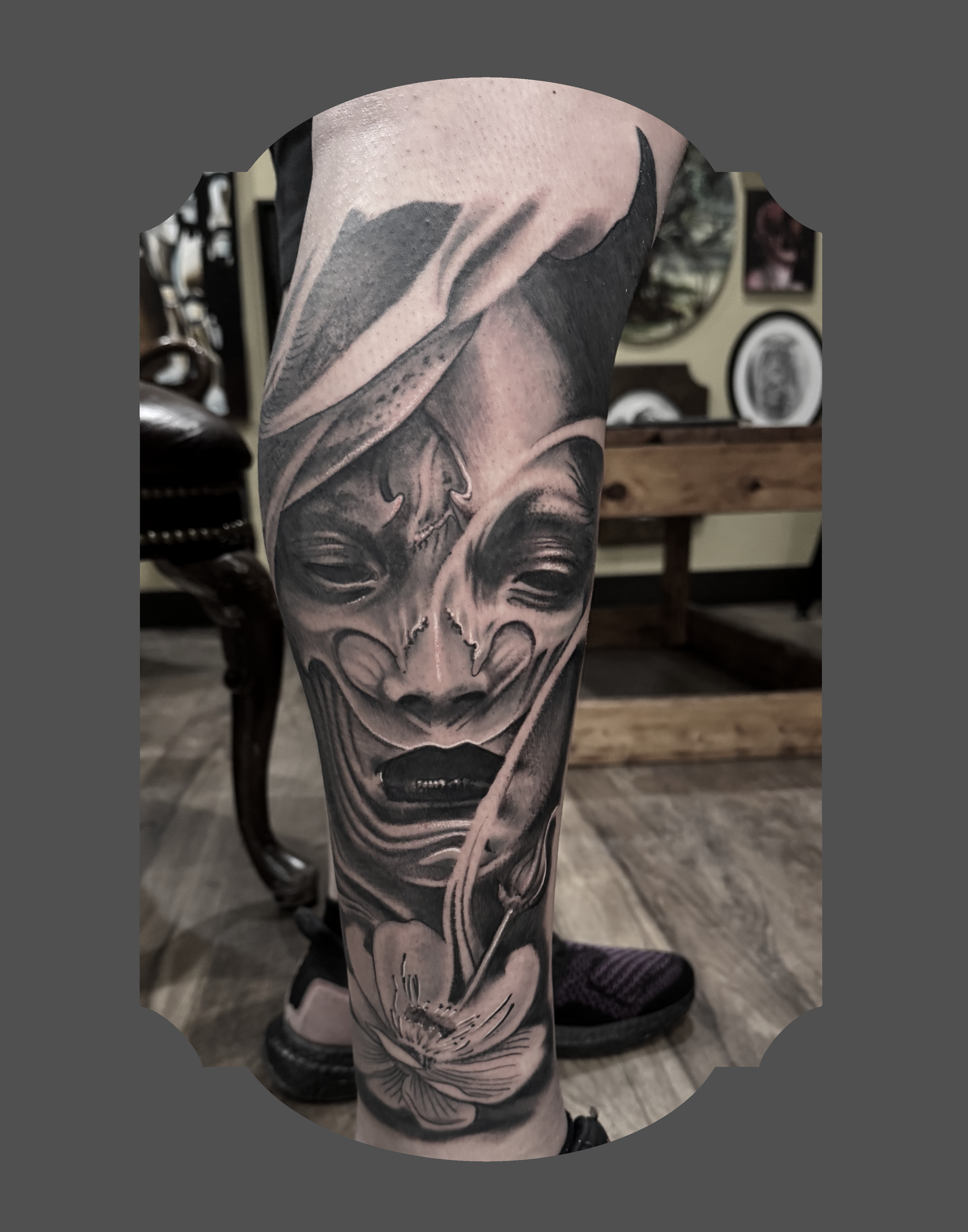 Black and gray tattoo of a woman's face with flowers on the leg.