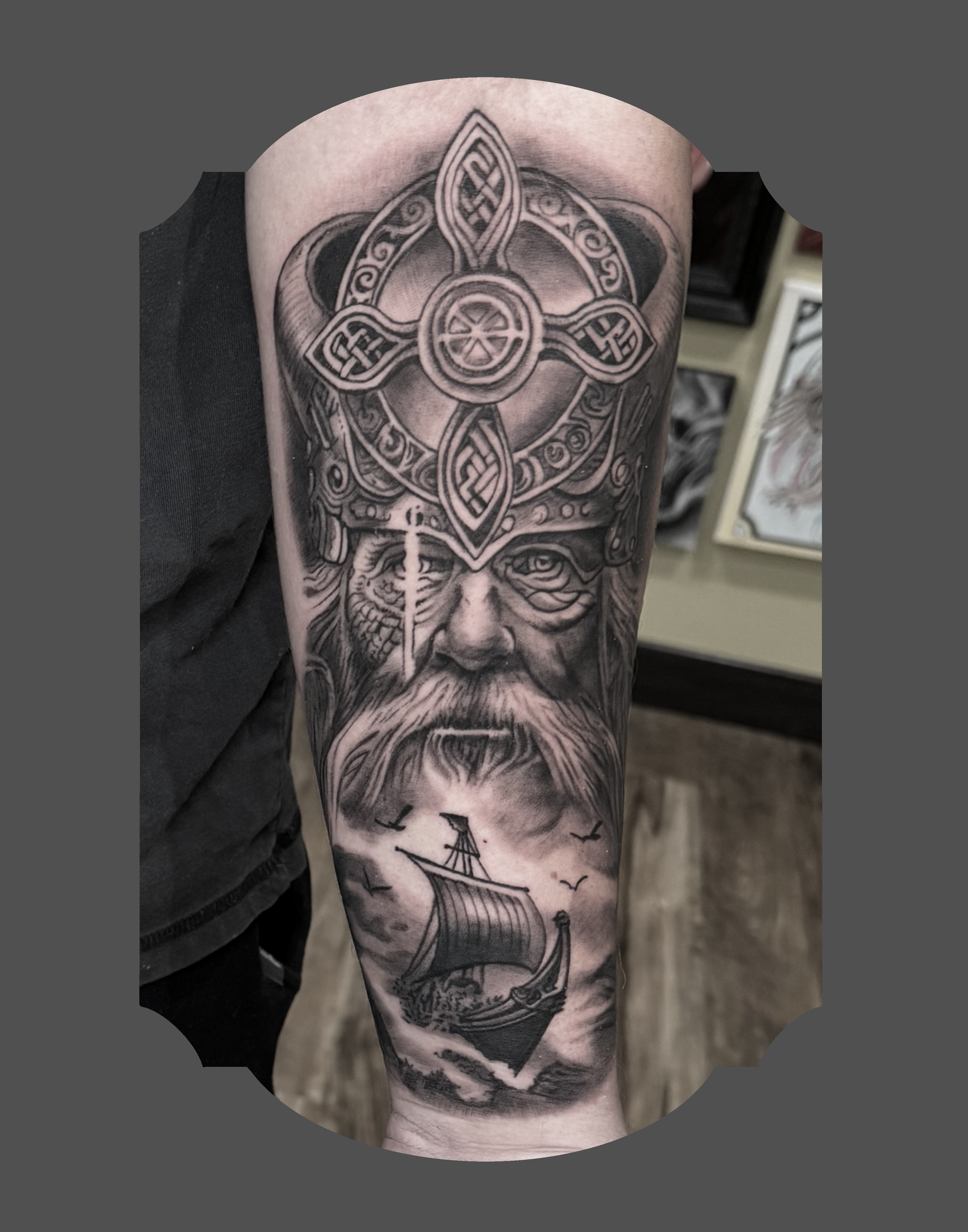 Black and gray tattoo of a Norse or Viking-inspired design covering most of a person's arm, including a ship with a sail, with birds flying above the ship.