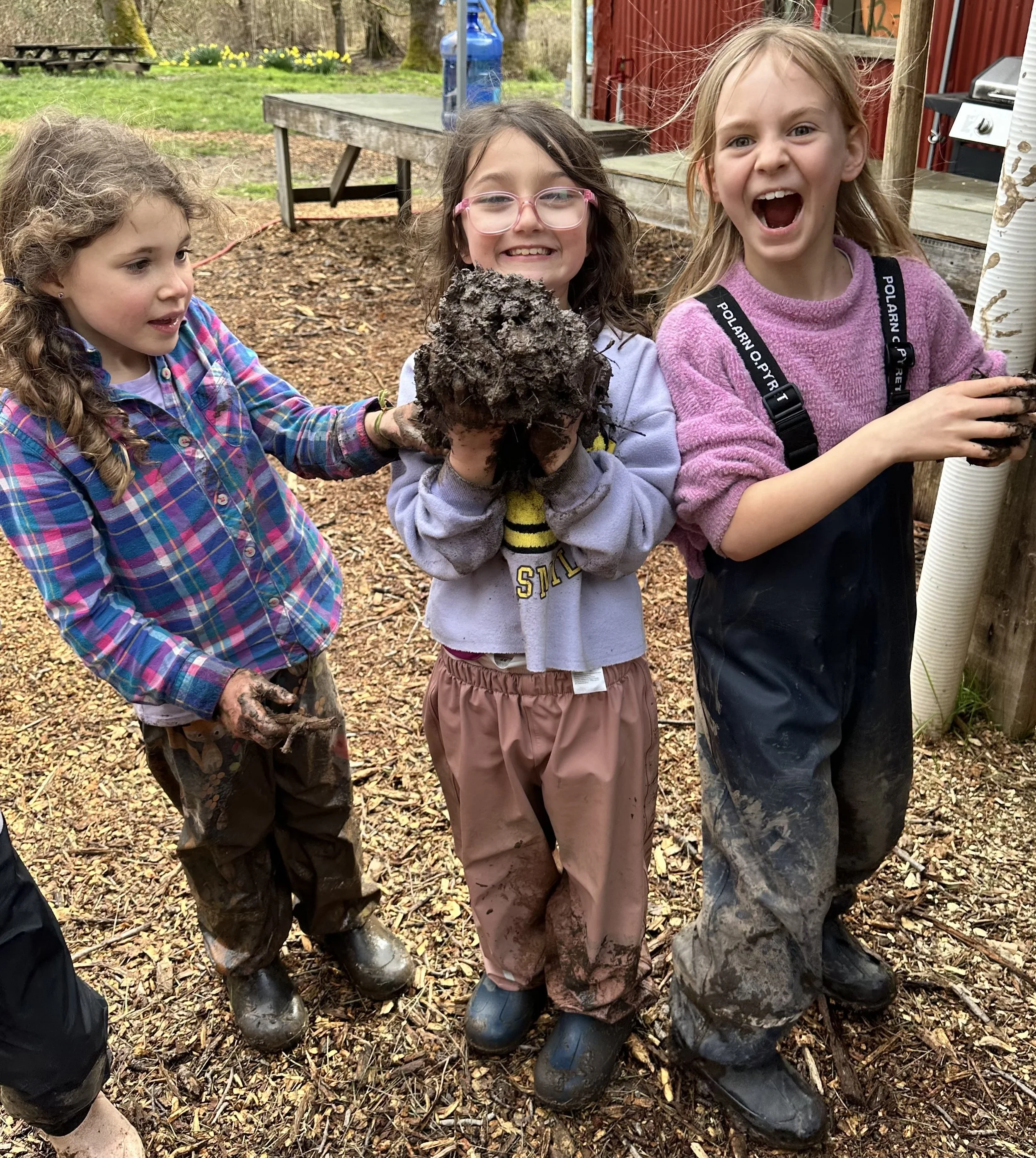 Three students playing with mud and laughing at the farm