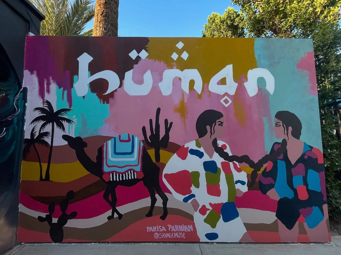 H&Uuml;MAN.
I created this mural for every layered being who&rsquo;s ever asked where they belong.

For those raised between languages, between deserts and borders, between the sacred and the surreal.

Two femmes&mdash;braided together&mdash;stand gr