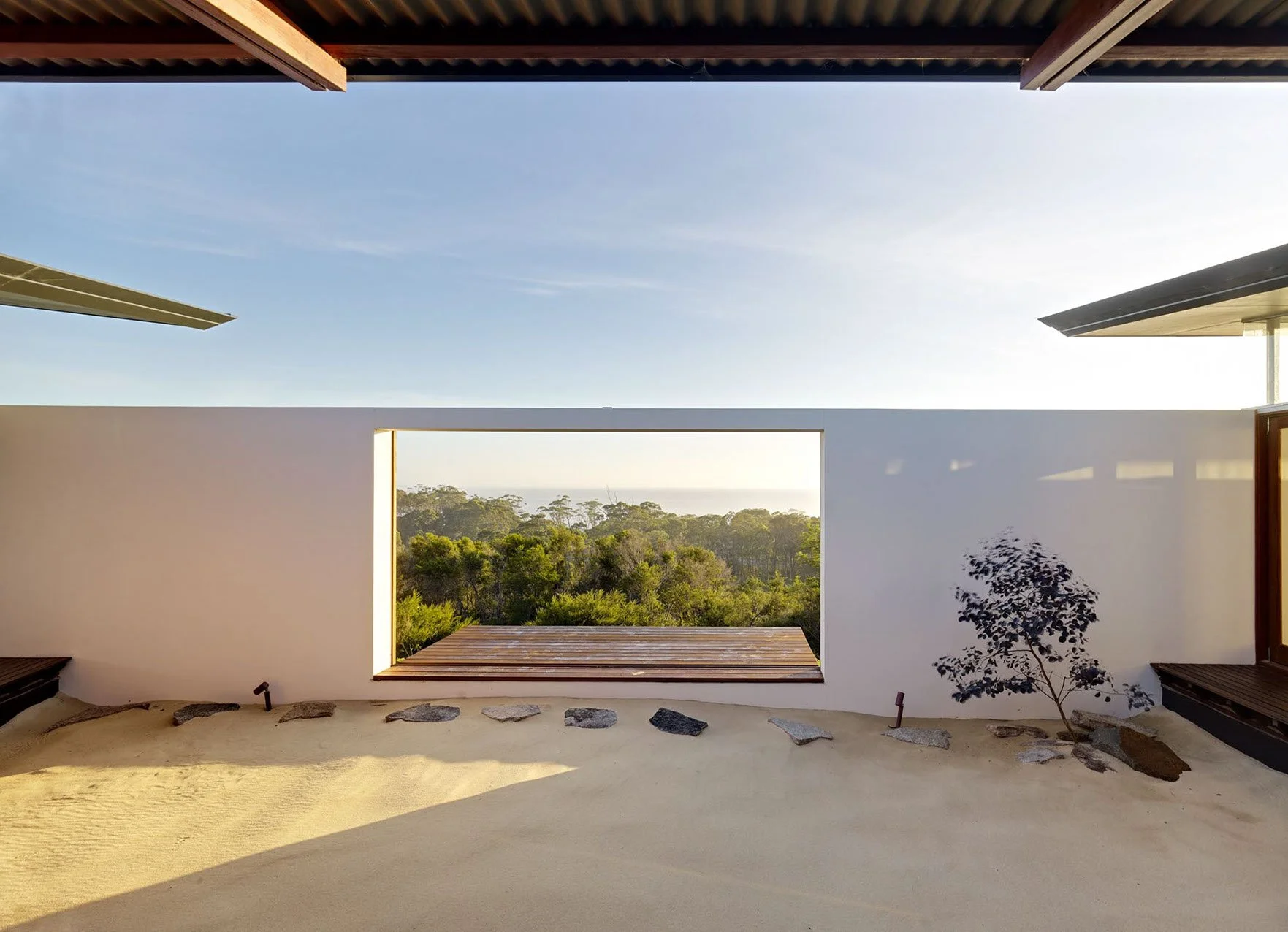 Modern house with large open window revealing a view of trees and sky beyond, with minimalistic interior design and a small plant in the corner.