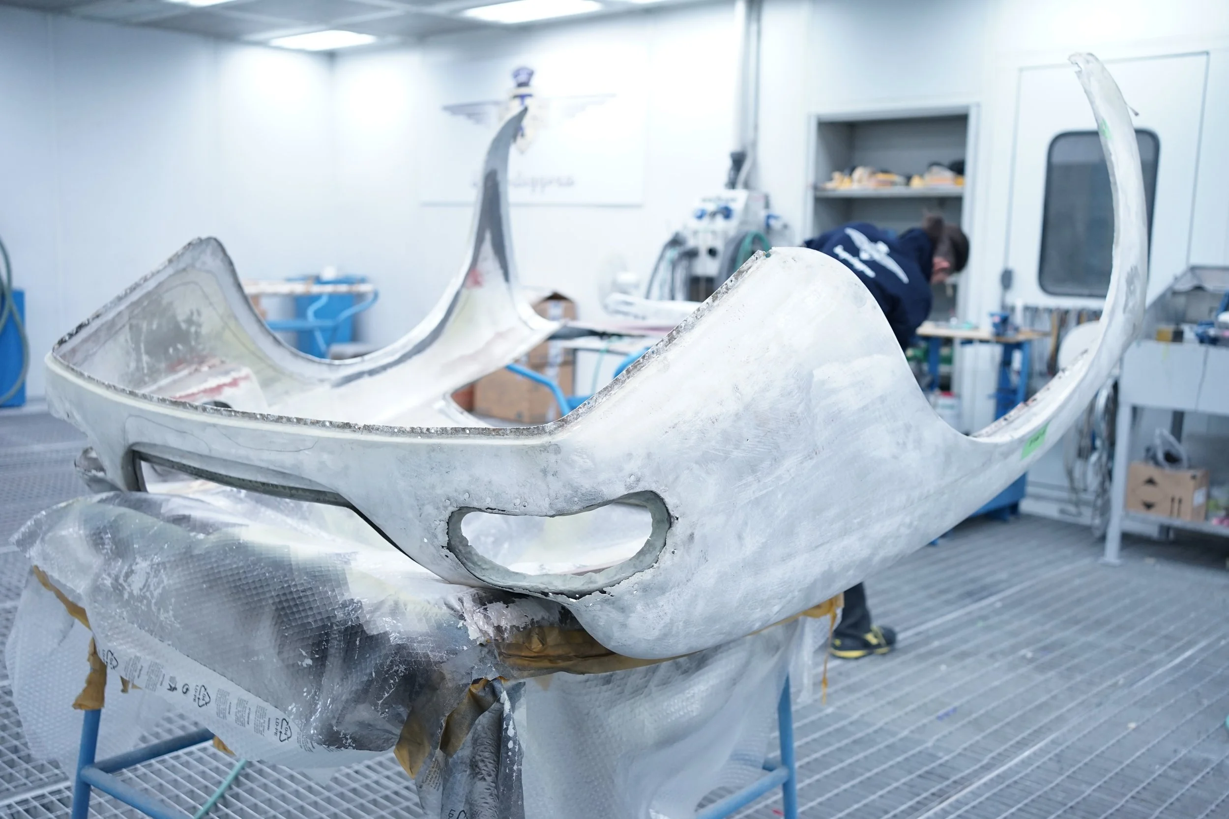 A bicycle frame under restoration or repair in a workshop, with a worker in the background working on other tools and equipment.