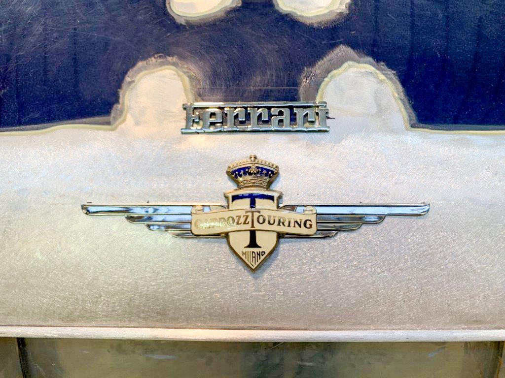 Close-up of vintage car badges, including Ferrari and Carrozzeria Touring Milano.