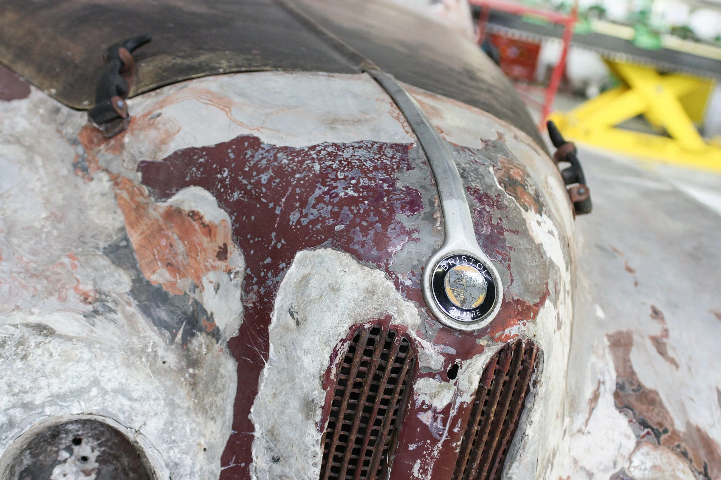 Close-up of an old, rusty vintage Bristol vehicle with peeling paint, rusted grills, and a faded badge.