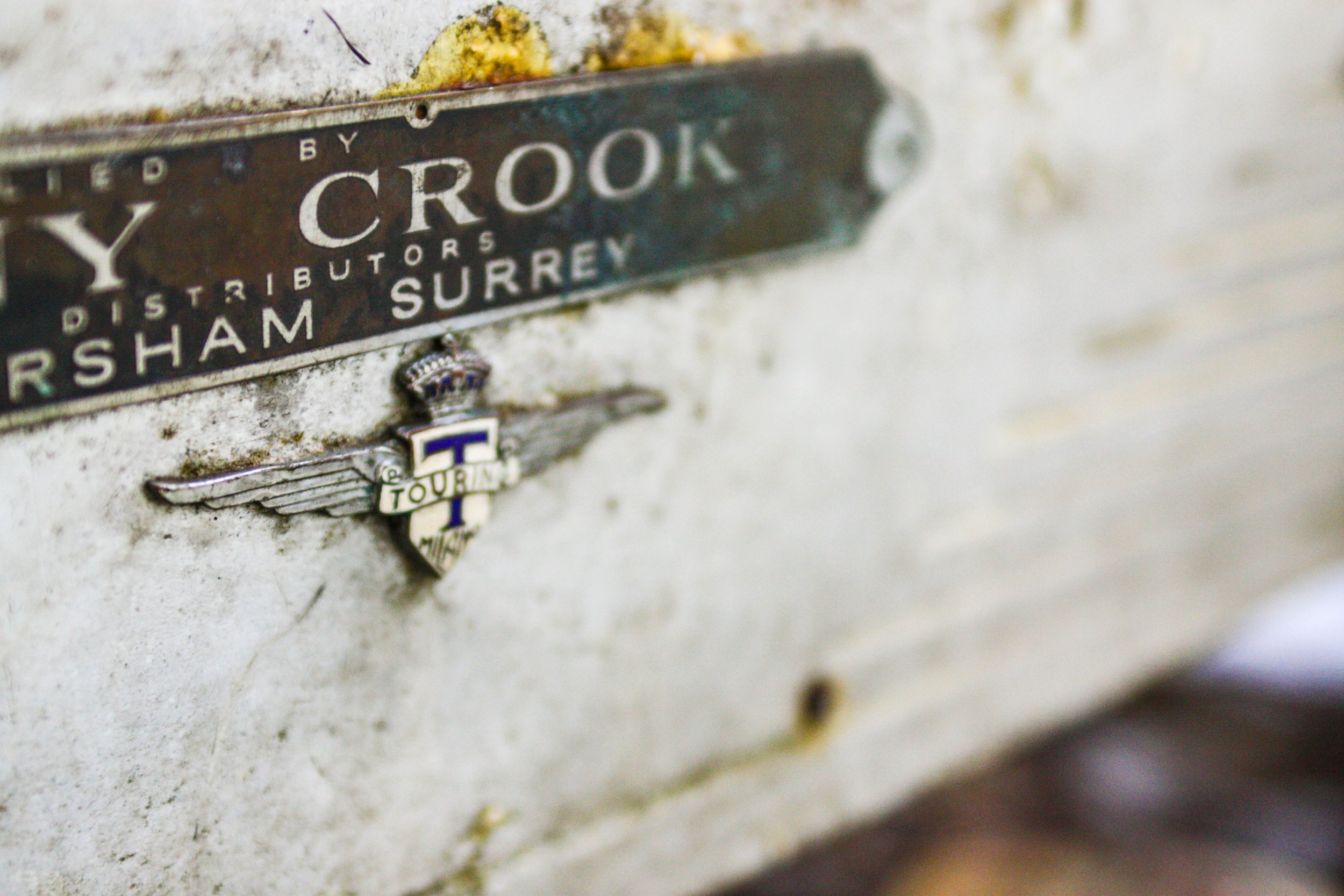 Close-up of a vintage metal sign displaying the address '73 Crook, Surrey,' with an emblem featuring a winged badge and a crown.