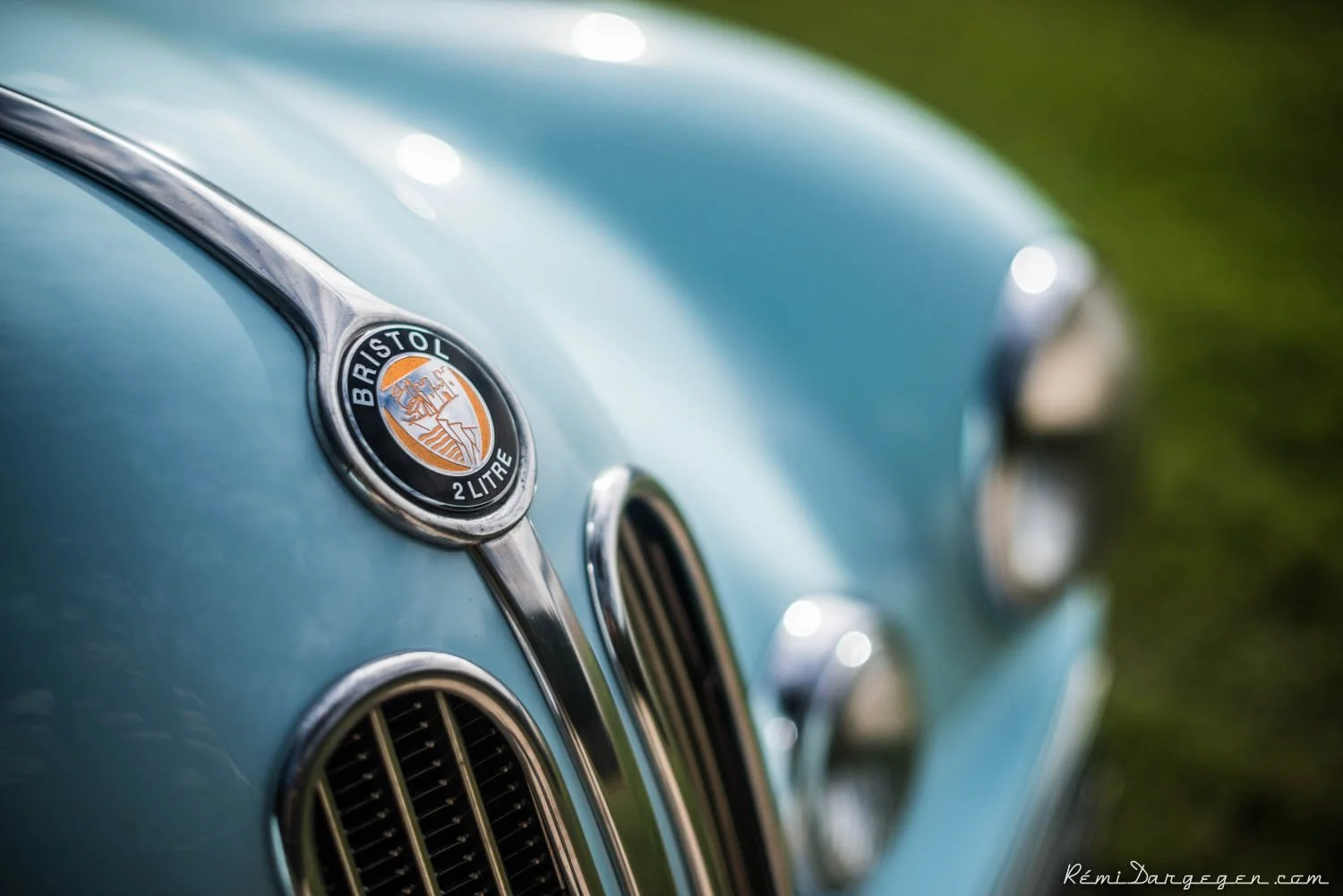 Close-up of the front of a vintage light blue Bristol 2 Litre car, showing a badge and part of the grille.