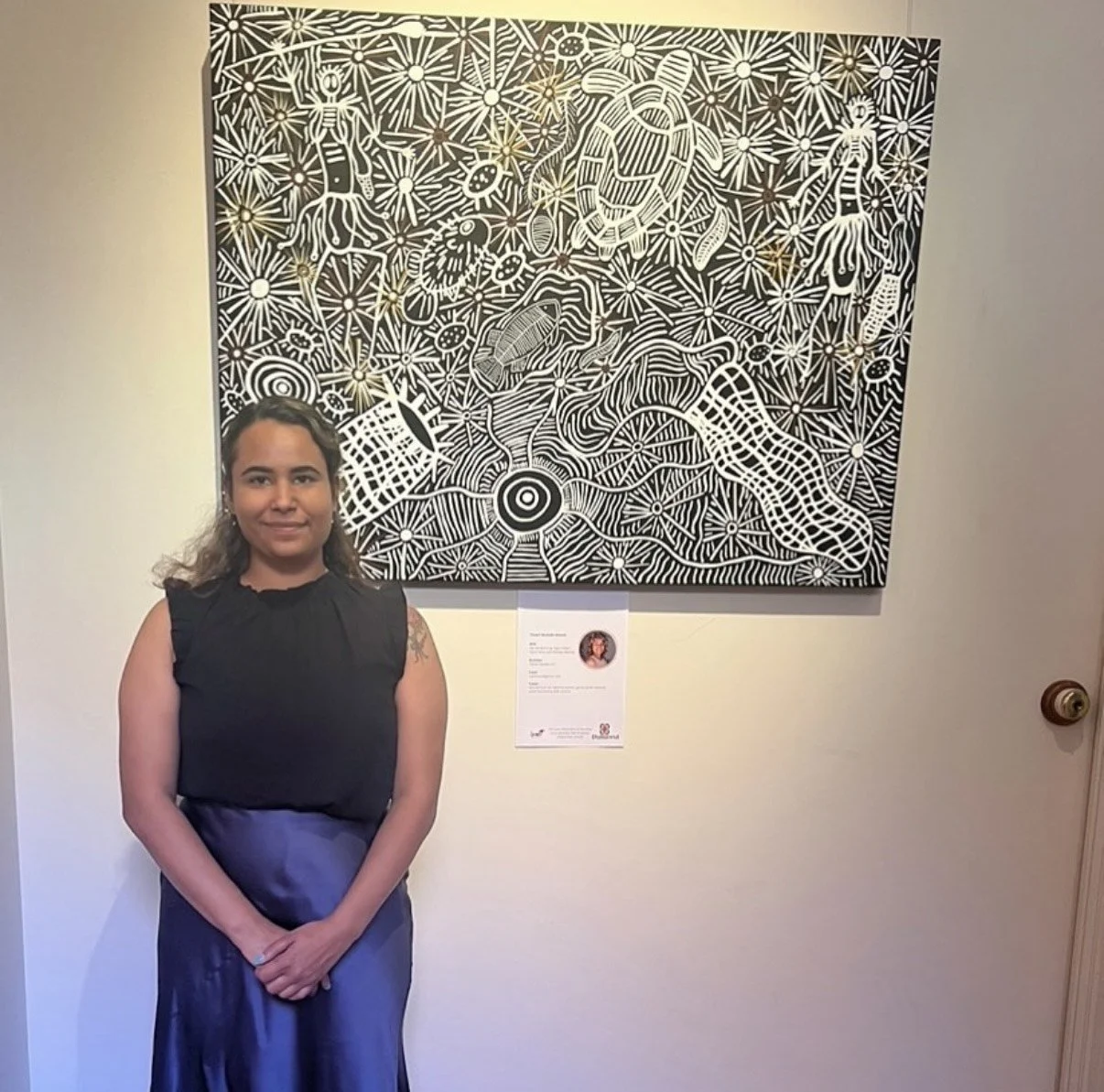 Woman standing in front of a large black and white abstract artwork with intricate lines and shapes.