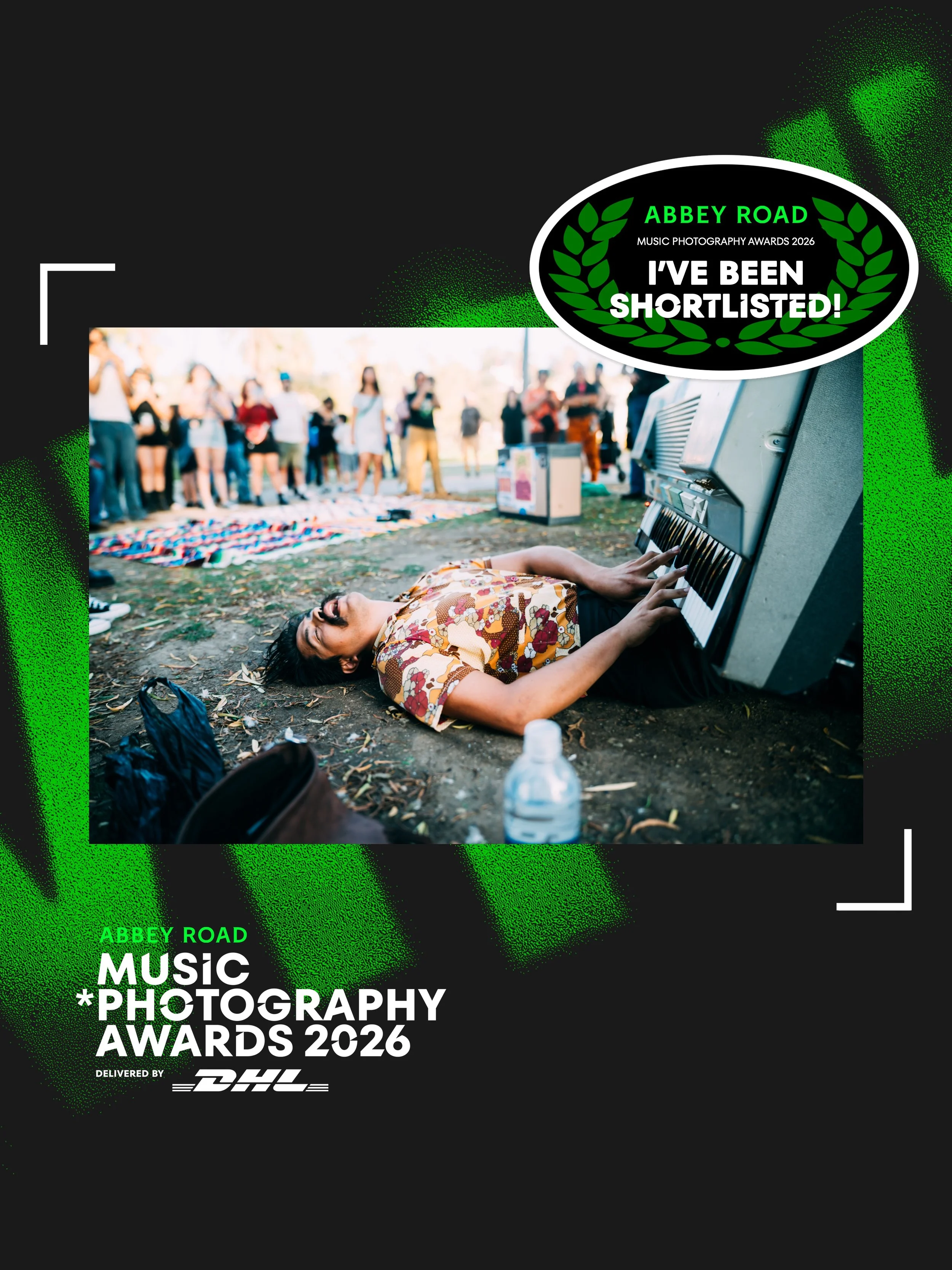A person with tattooed arms lying on the ground playing an keyboard at an outdoor music event with a crowd of people in the background and event advertising text overlayed.