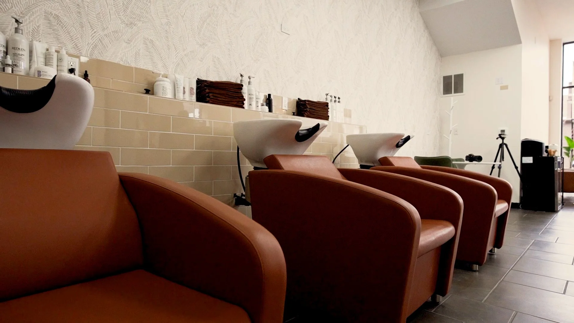 Interior of a hair salon with brown leather shampoo chairs, wash basins, and hair care products on shelves.