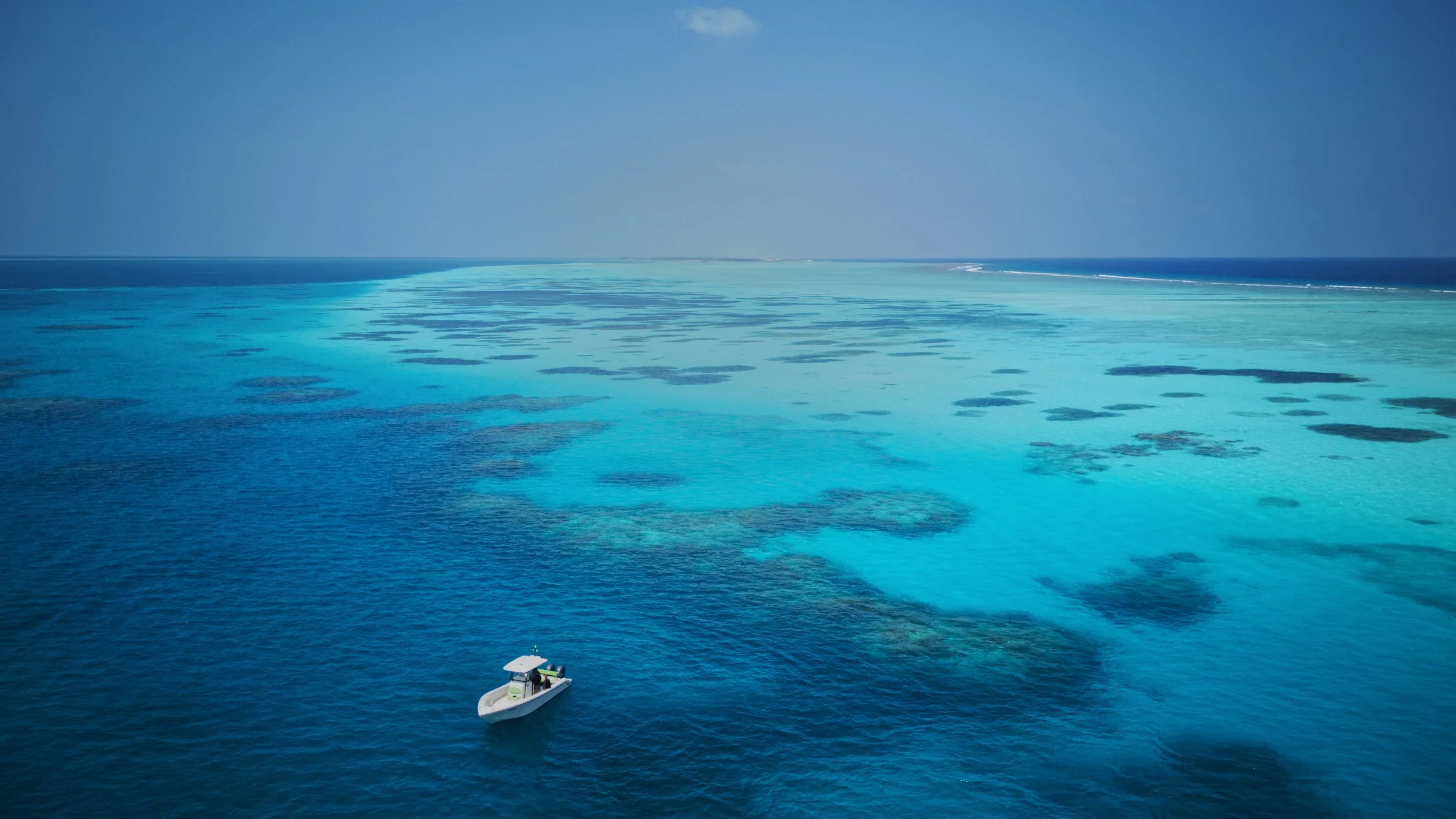 Drone photo of a speedboat on the clear, calm blue and turquoise ocean of a remote Atoll in the Maldives.