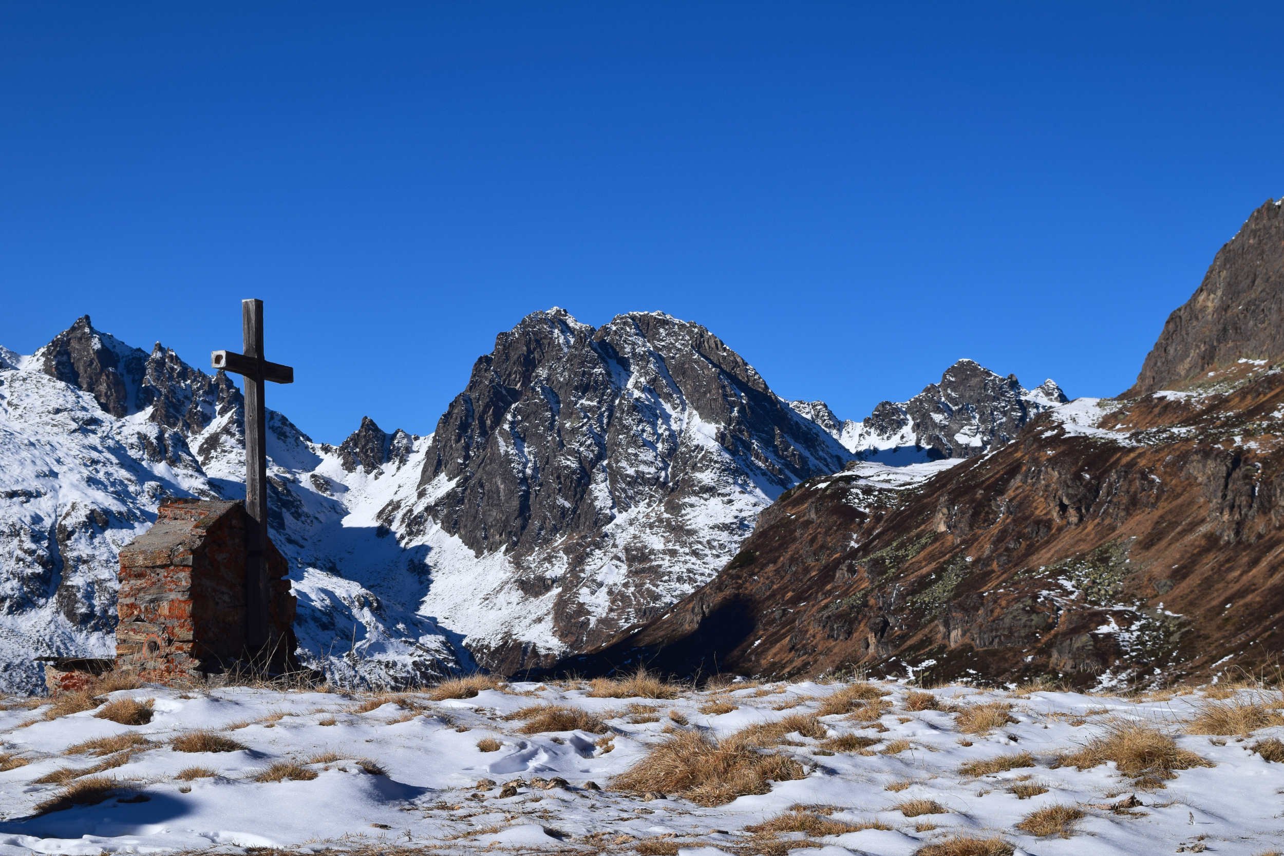 Landscape photo of a Christian shrine or church with a crucifix cross surrounded by the snowy mountains of the Swiss Alps.