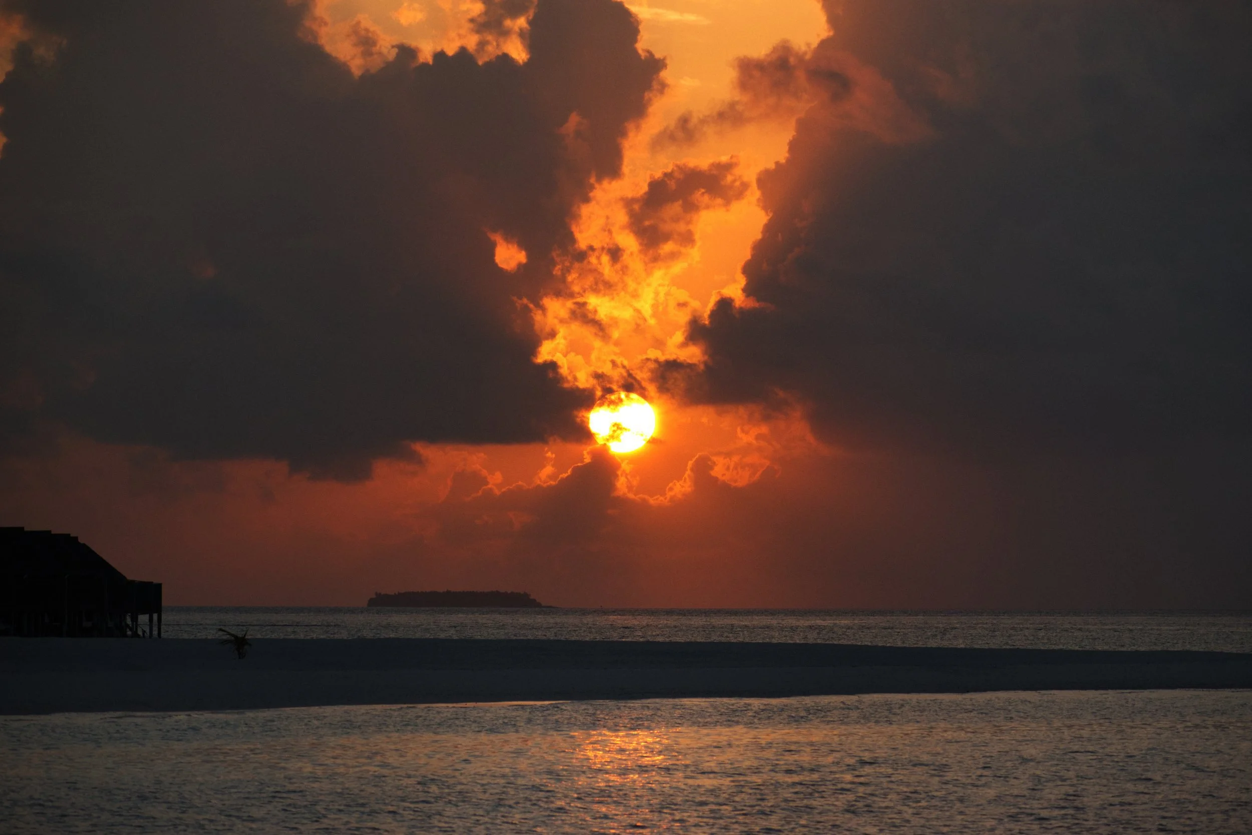 Photo of a fiery red sunset with dramatic clouds at a luxury resort in the Maldives, taken with a telephoto zoom lens.