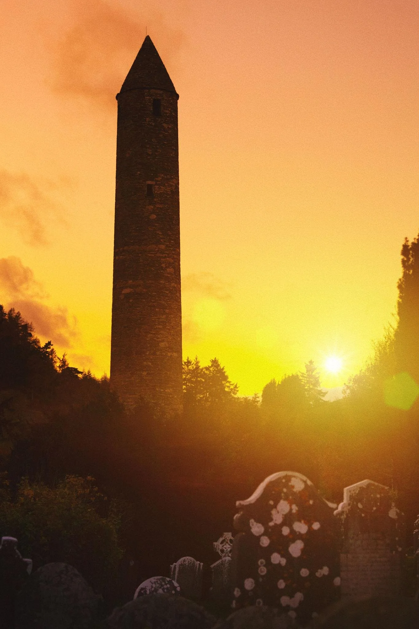 Round tower at Glendalough at sunset with graveyard and warm evening light