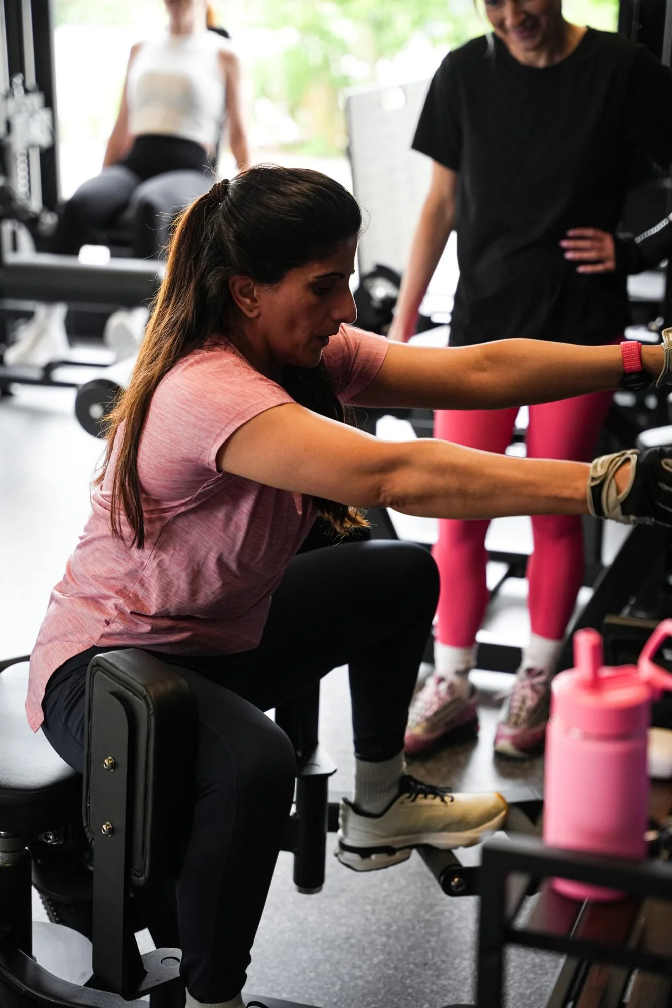 Member on a seated row machine with a coach supervising at Physique Pro Great Park
