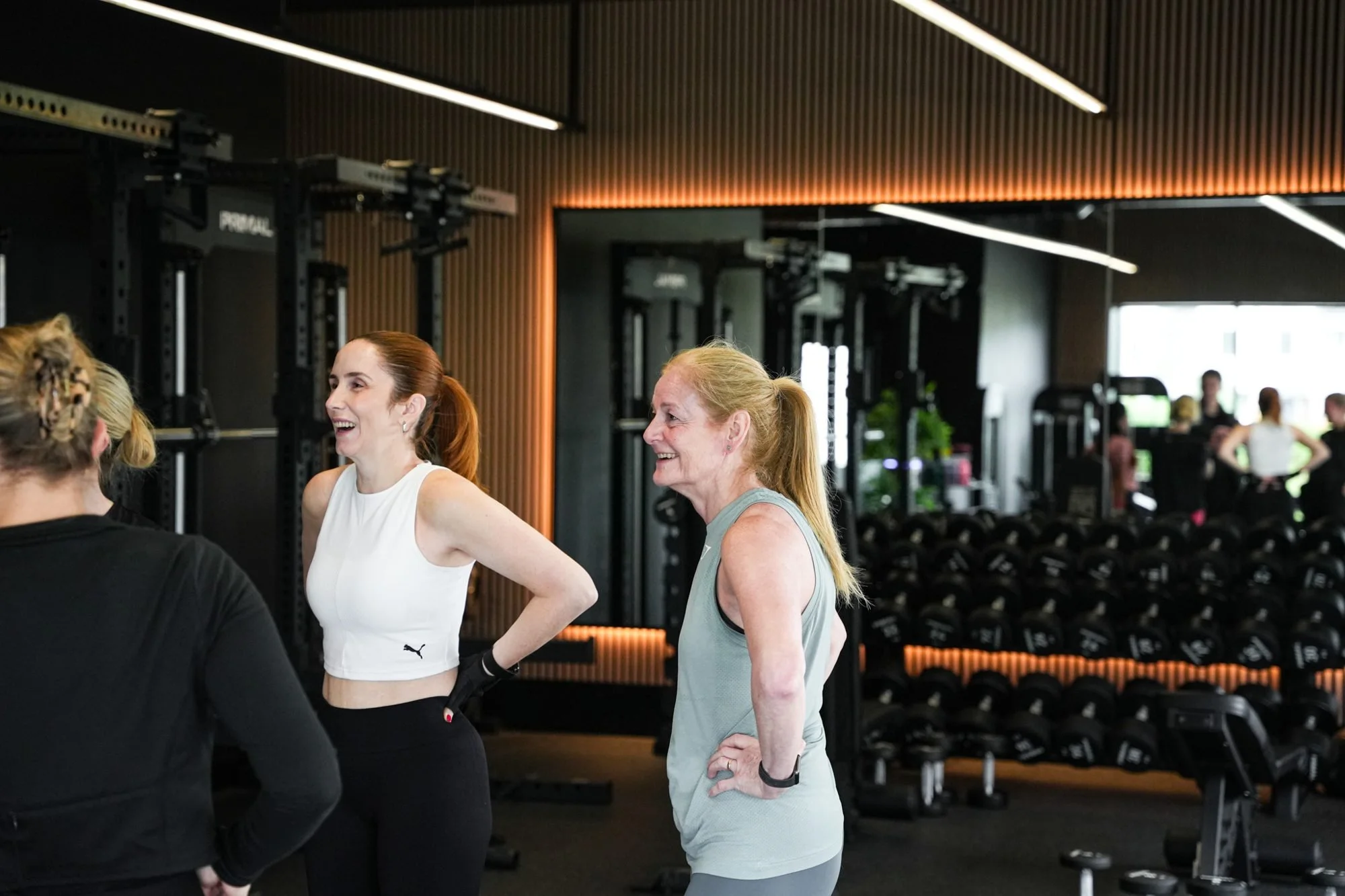 Members chatting on the gym floor in front of the dumbbell rack at Physique Pro Great Park