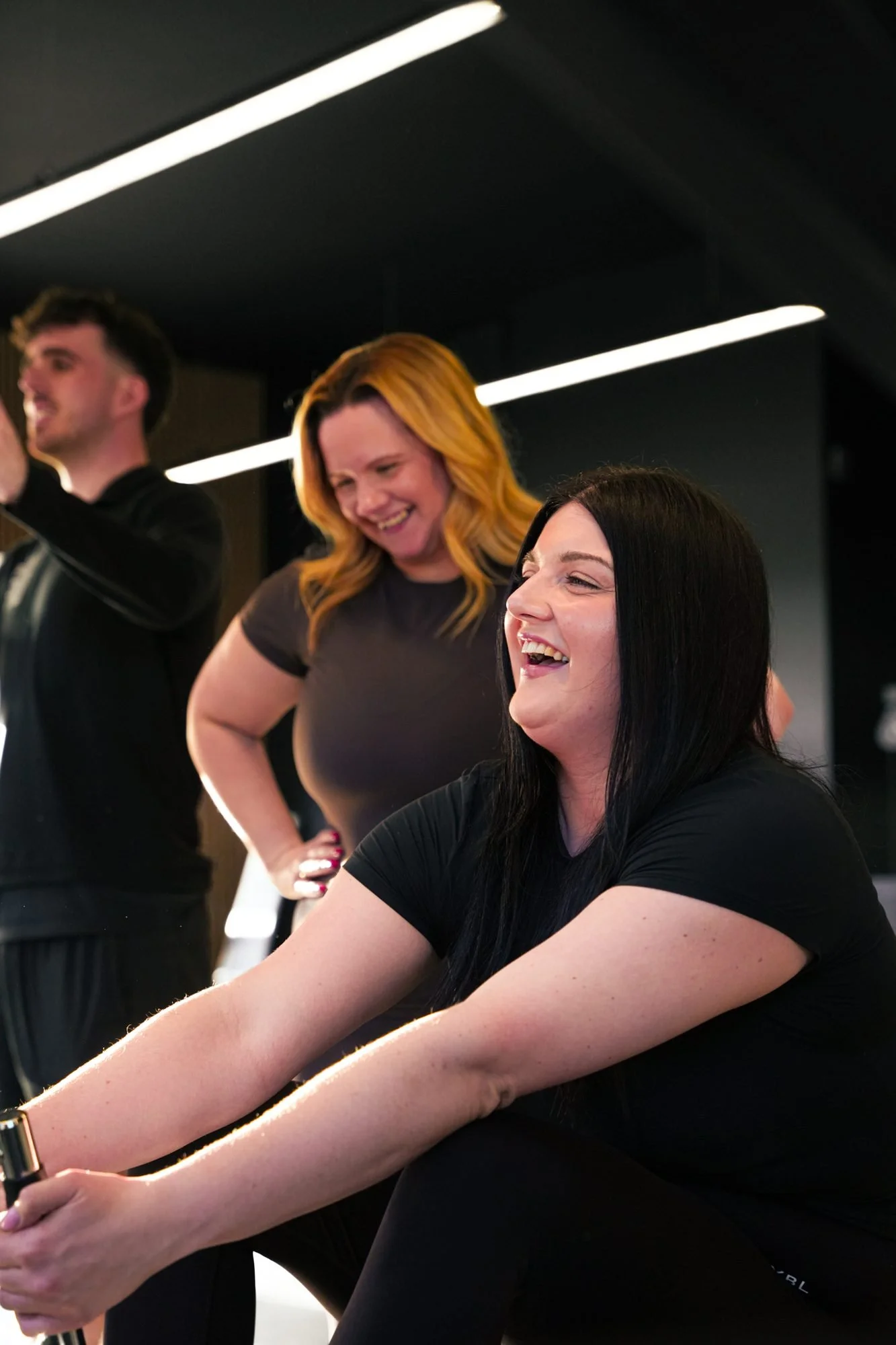 Members laughing together on a rowing machine at Physique Pro Great Park