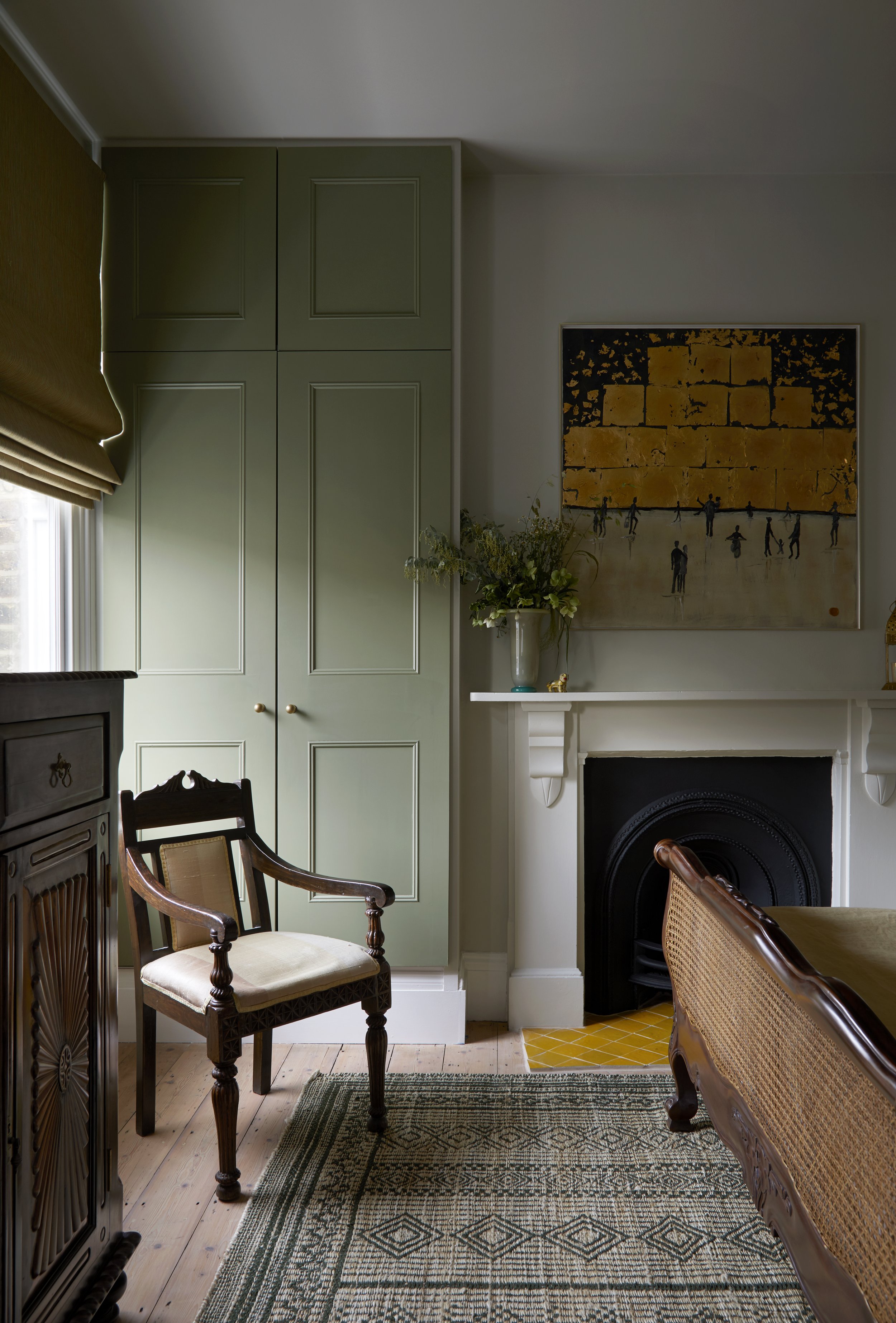 A refurbished  room for guests, a patterned rug, green cupboards, , a painting above the fireplace, and a vase with flowers on the mantel.