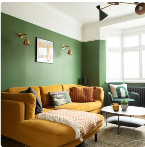 Living room with green wall, mustard yellow sofa, throw pillows, a white coffee table, and a green armchair near a window.
